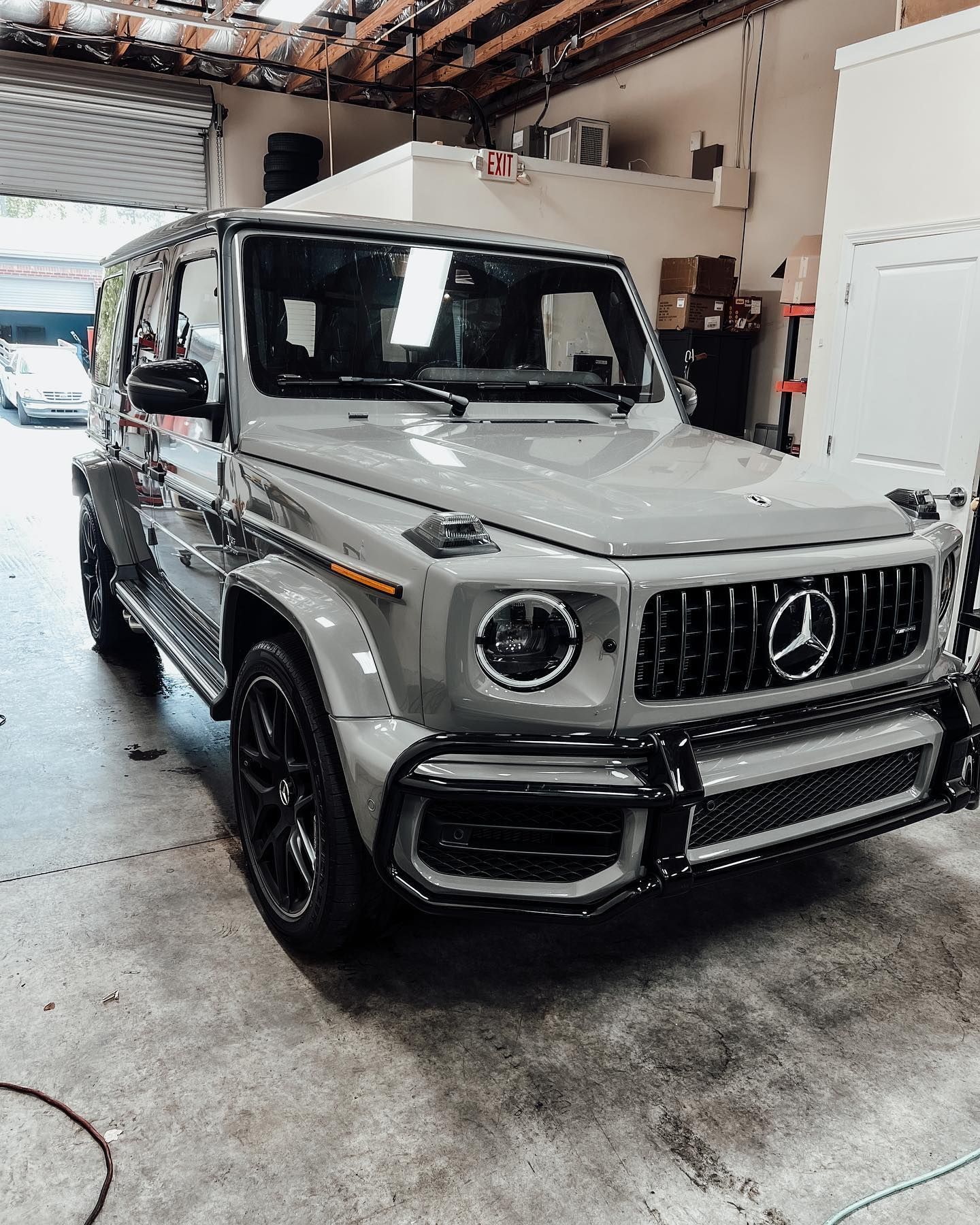 A glossy, cement-gray Mercedes-Benz G-Wagon parked inside an auto shop with black wheels and a black grille.