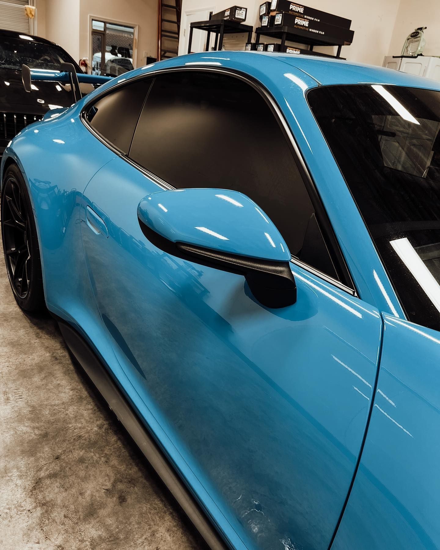 A bright blue sports car parked in a garage, focusing on the side profile, door mirror, and tinted window.