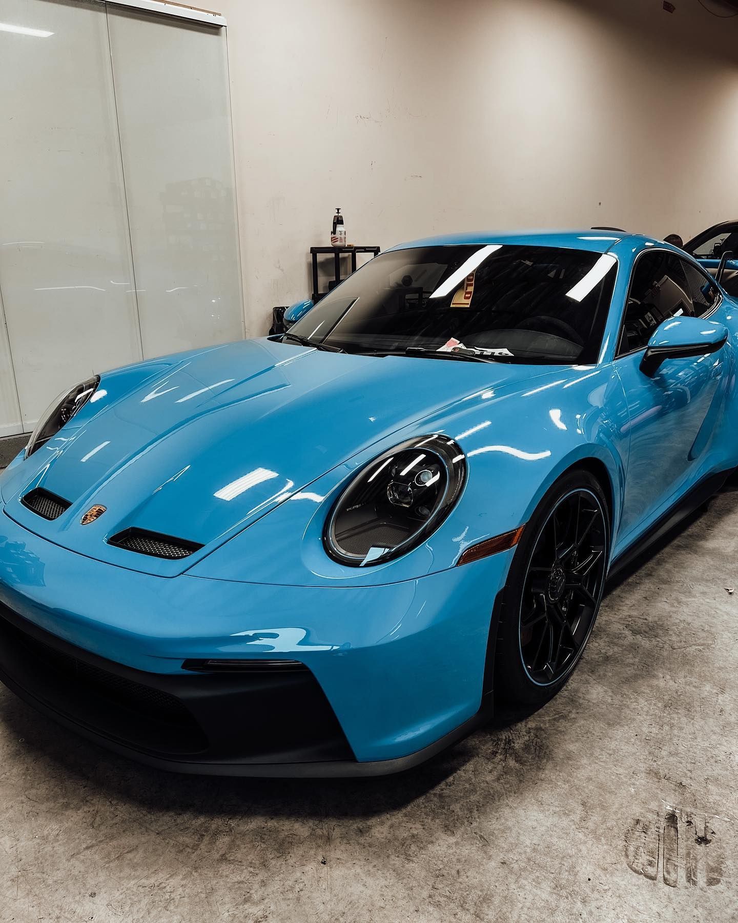 A grey Porsche 911 parked inside a garage with bright overhead lighting.