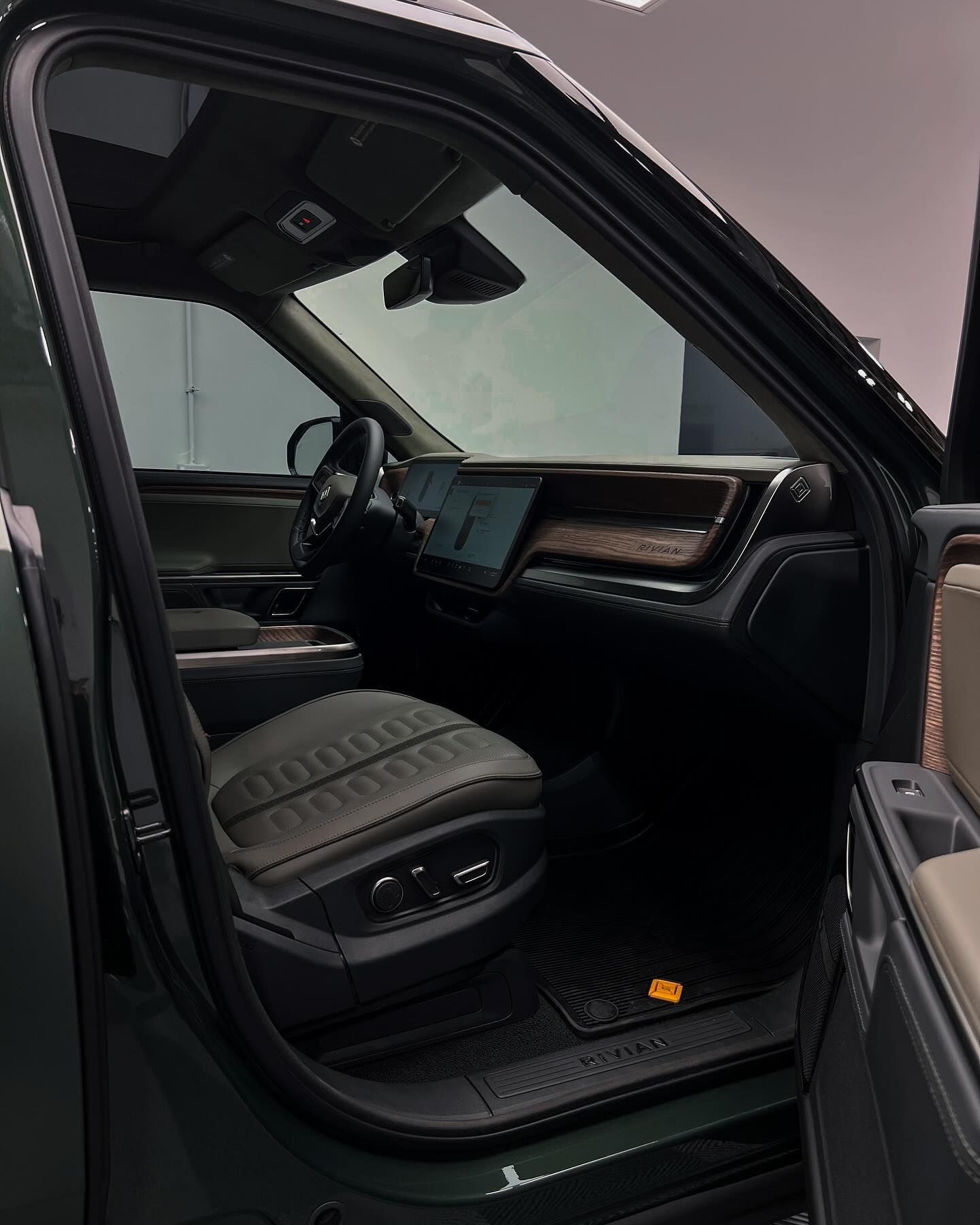 View into the interior of a dark-colored SUV, showcasing leather bucket seats, a dashboard screen, and wood-grain trim.