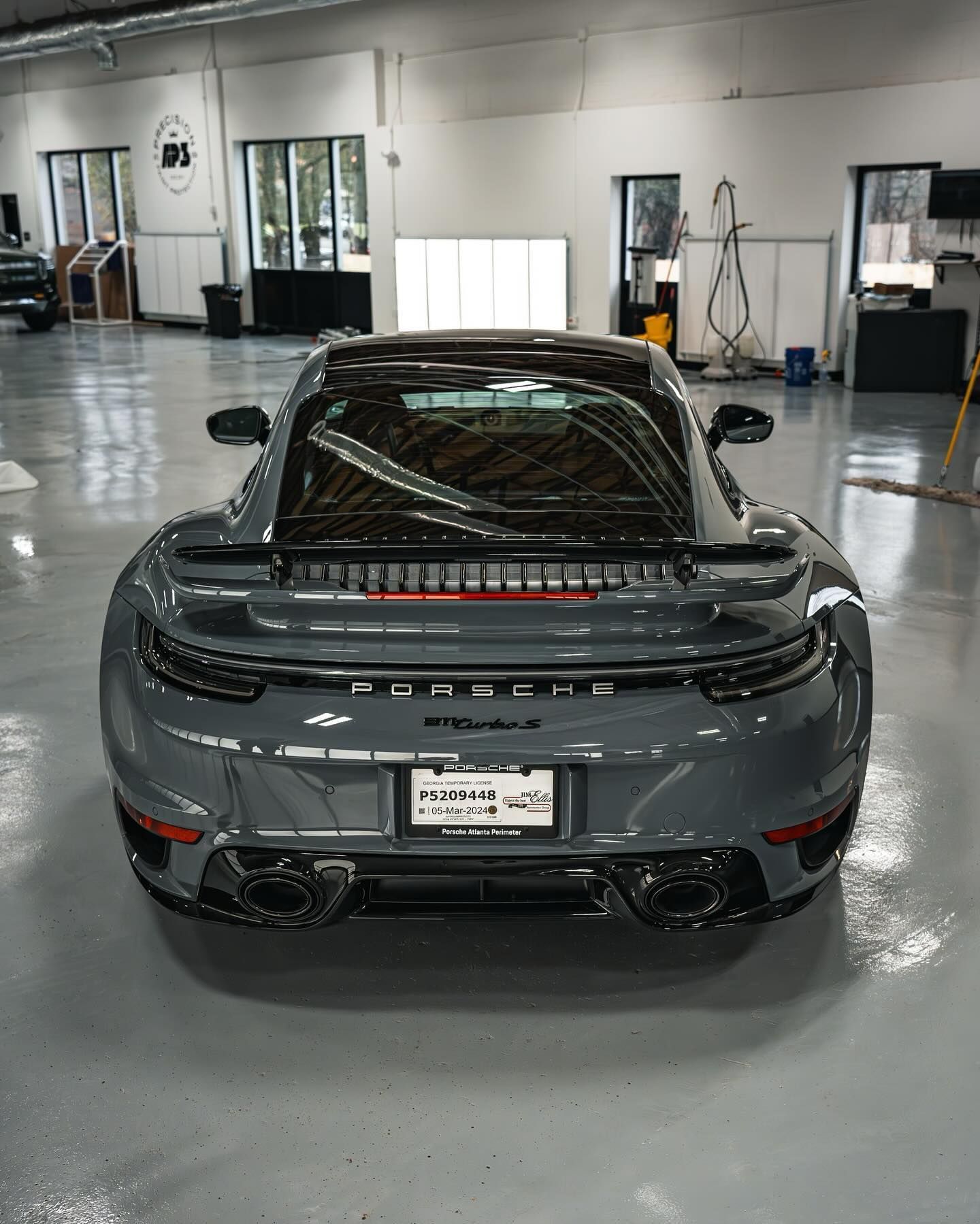 A grey Porsche 911 Turbo S parked inside a brightly lit car detailing garage with a glossy floor.