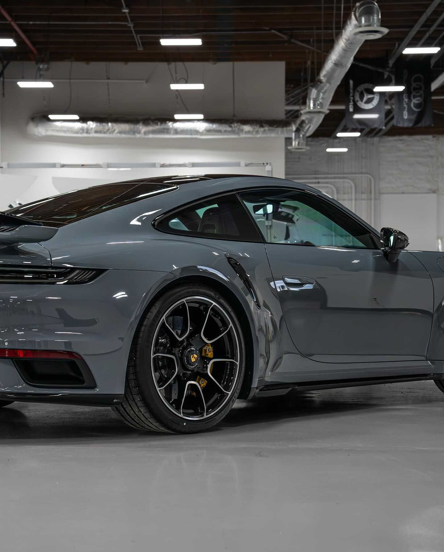 A sleek gray Porsche 911 Turbo S parked inside a modern, industrial-style garage with high ceilings and bright lights.