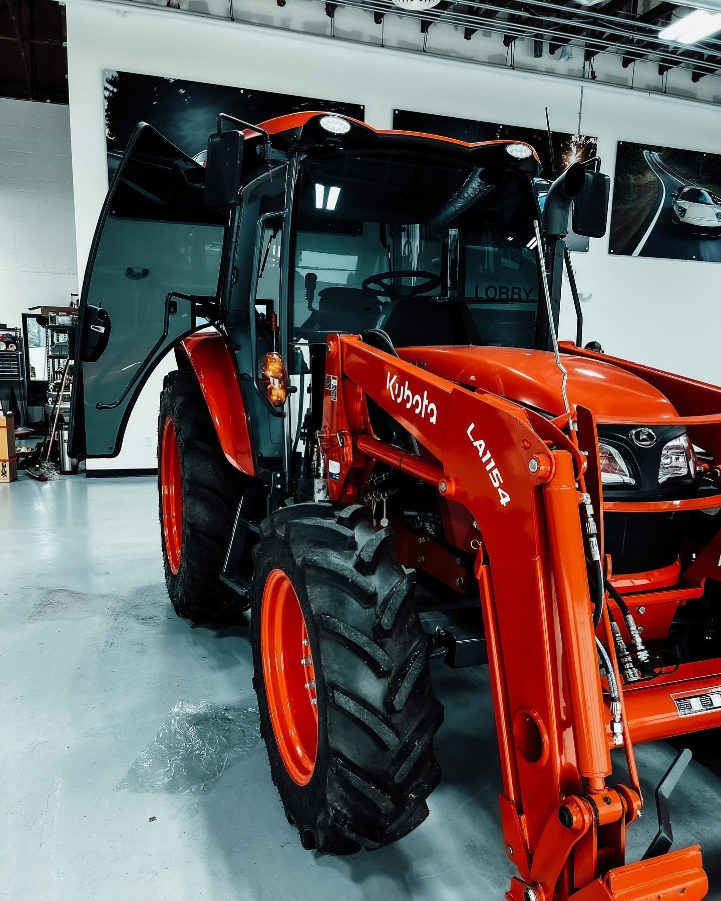 An orange Kubota tractor with a front-end loader parked indoors on a white floor.