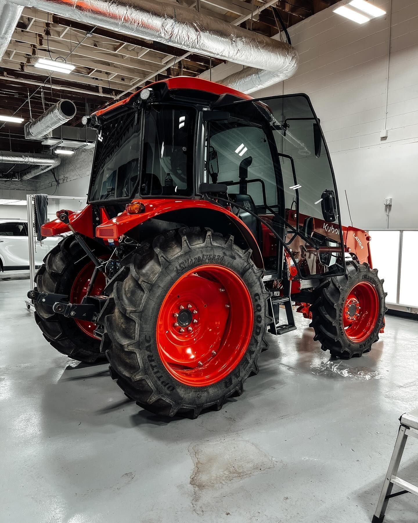 A red tractor with a closed cab parked inside a brightly lit industrial garage.