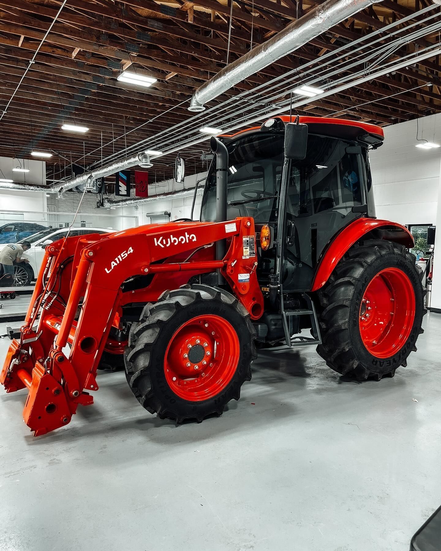 An orange Kubota tractor with a front-end loader parked inside a bright, industrial garage.