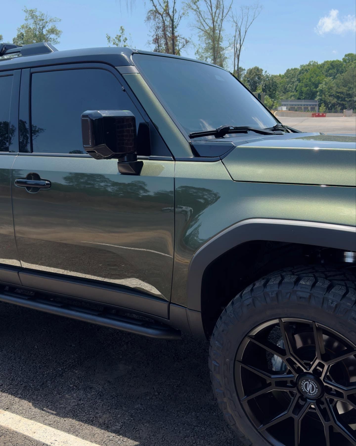 A dark olive green SUV with black off-road wheels and tinted windows parked on an asphalt lot.