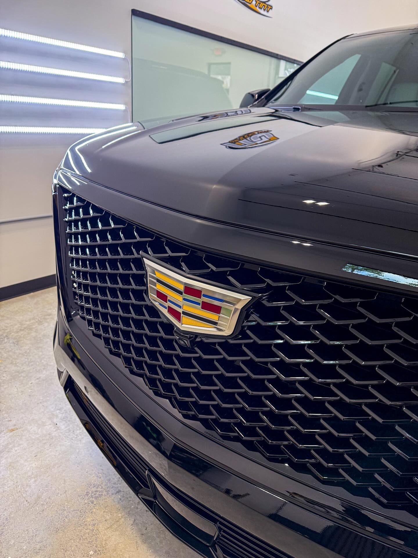 A close-up, angled view of a black Cadillac SUV front grille with a prominent, colorful Cadillac emblem.