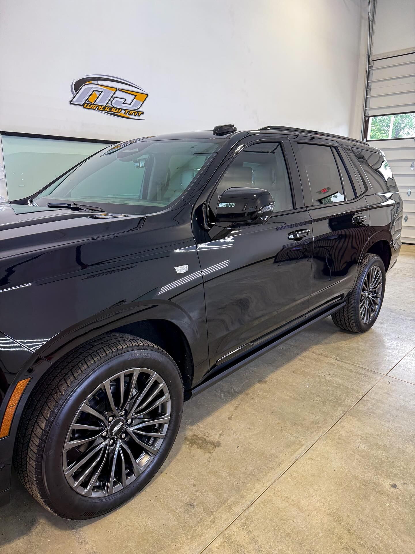 A shiny black Cadillac SUV parked inside a bright, clean garage with a logo on the wall.