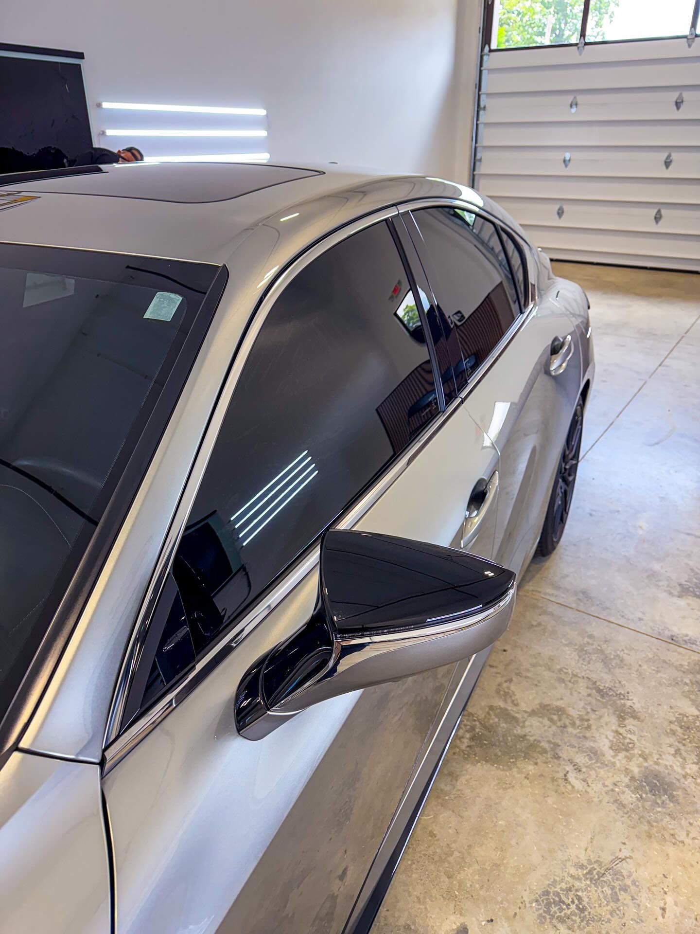 A silver sedan parked in a garage with dark tinted windows, a sunroof, and a black side mirror.