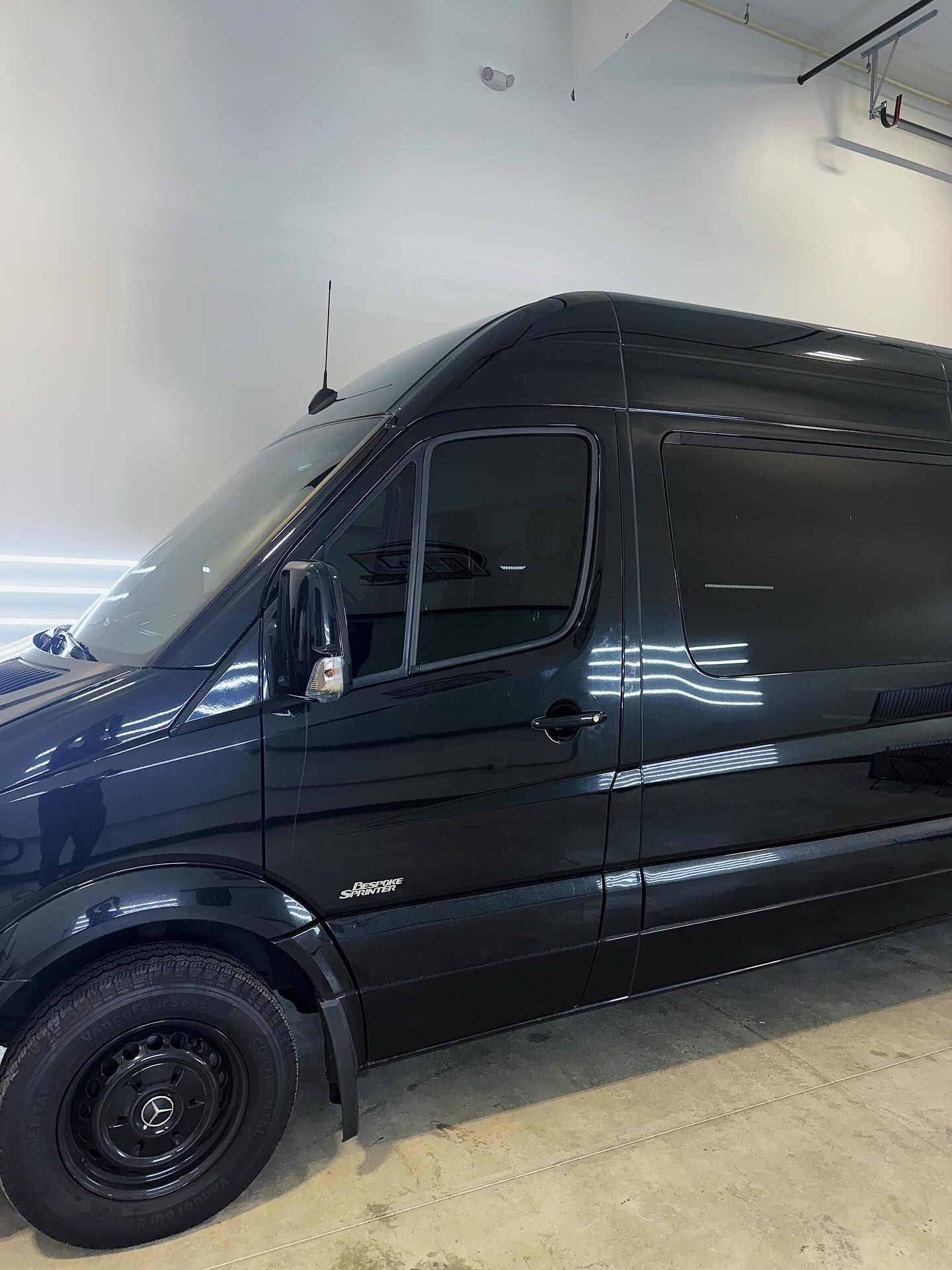 A shiny black commercial van parked indoors on a concrete floor, viewed from the front passenger side.