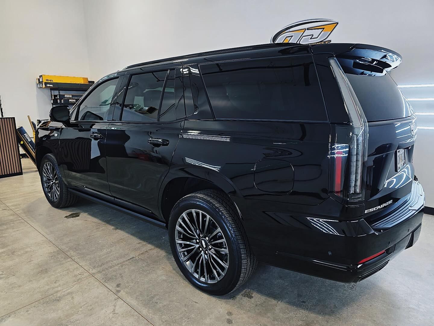 A black Cadillac Escalade SUV parked in a garage, showcasing its rear and side profile, large rims, and tinted windows.