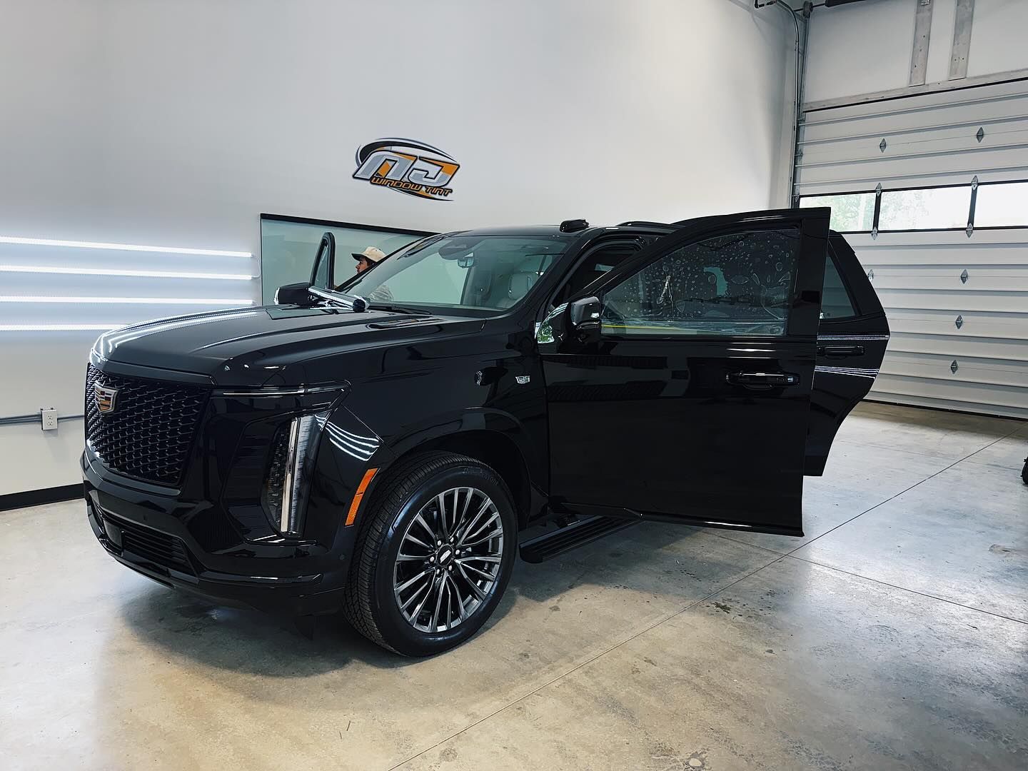 A sleek, black Cadillac SUV parked inside a well-lit garage with its front driver-side door open.