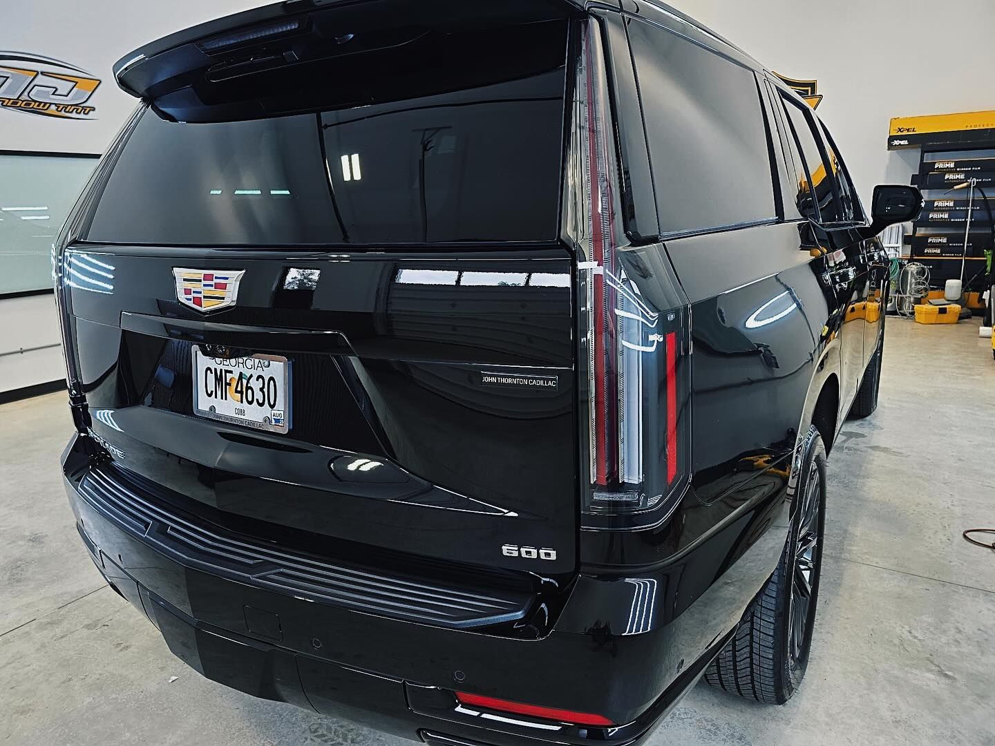 A rear view of a glossy black Cadillac Escalade SUV parked in a garage, showcasing its signature vertical taillights.