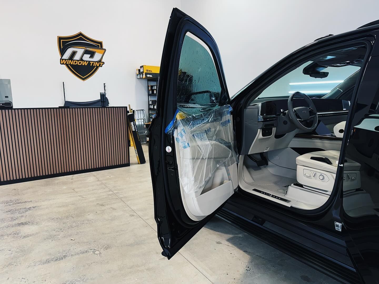 A car door open in a workshop, showing the interior with light-colored seating and a protected window.