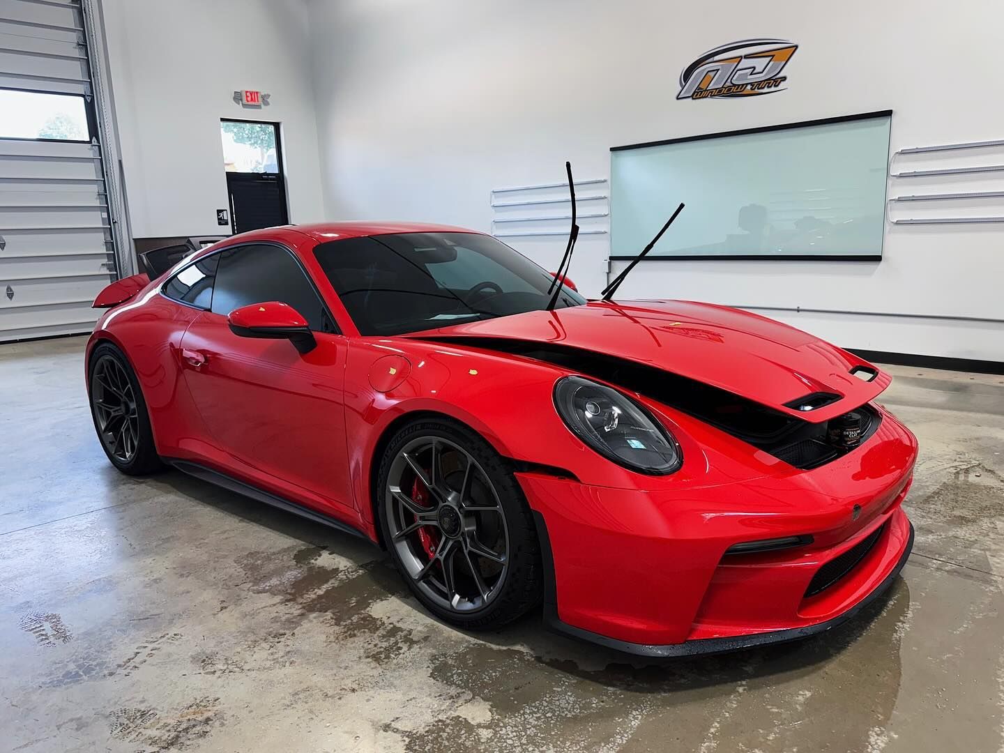 A bright red Porsche 911 GT3 with its hood open in a brightly lit, industrial-style garage or workshop.