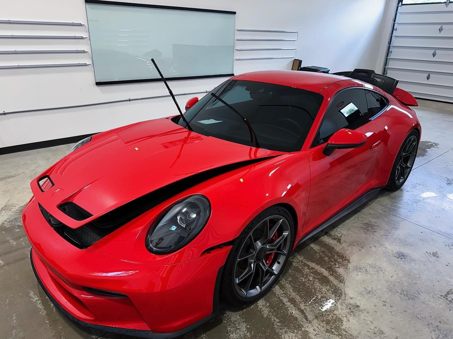 A bright red Porsche 911 GT3 with its front hood slightly raised, parked inside a brightly lit garage.