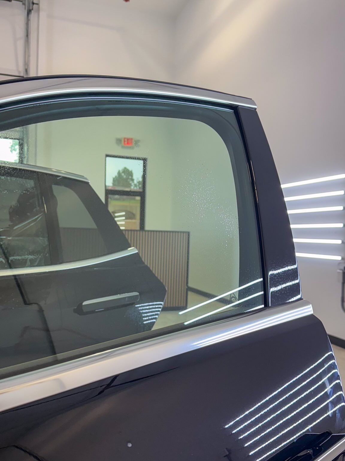 A view looking through a vehicle’s window at an interior workshop space with a red exit sign visible on the back wall.