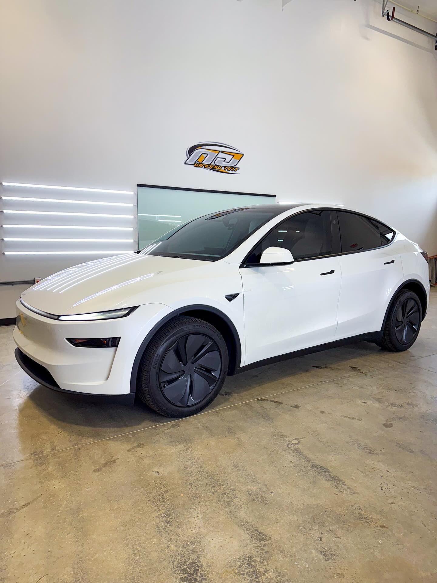 A white Tesla Model Y parked in a bright, modern indoor garage with dark rims and tinted windows.