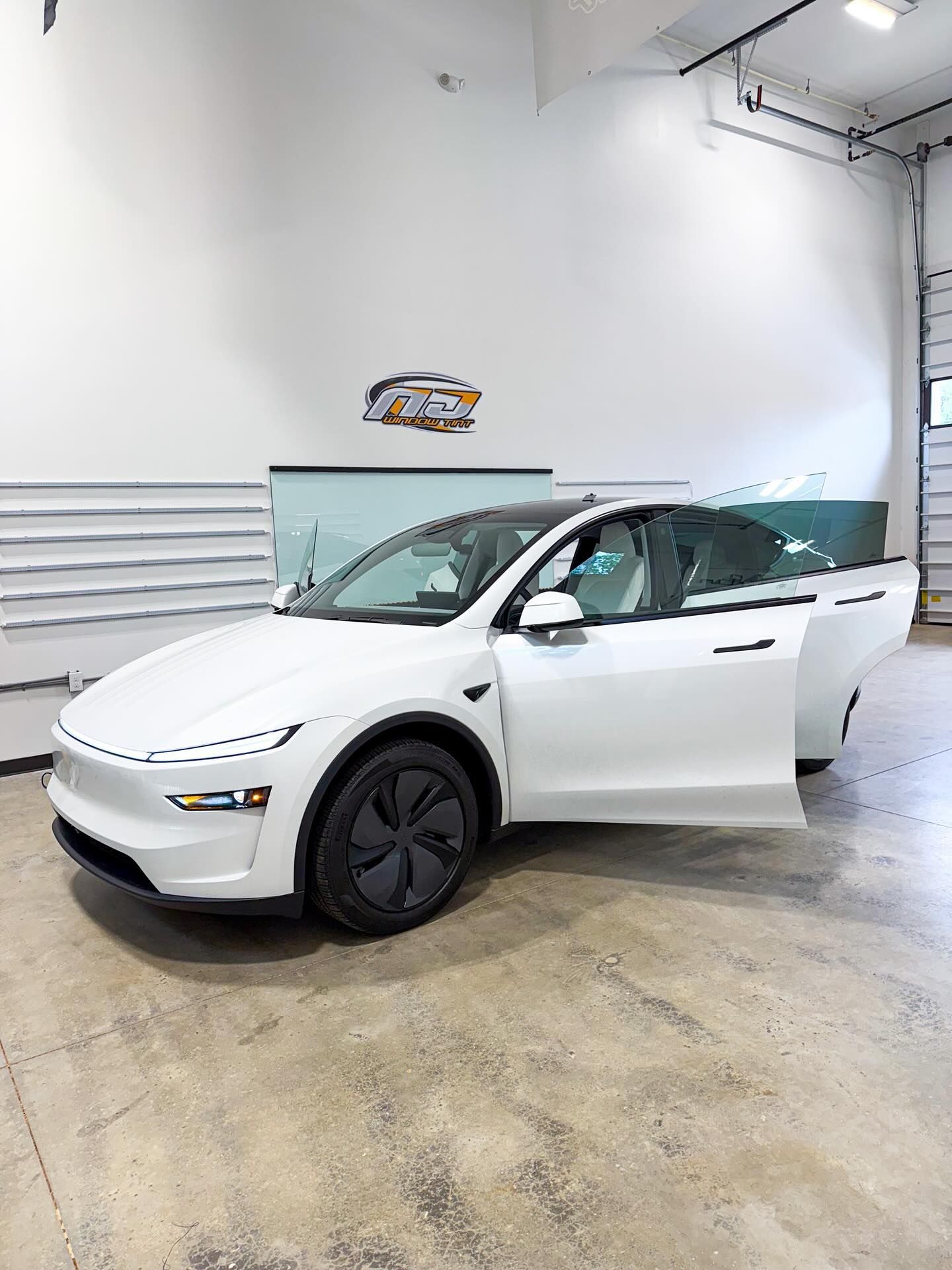 A white Tesla Model Y with its front door open parked in a brightly lit indoor showroom.
