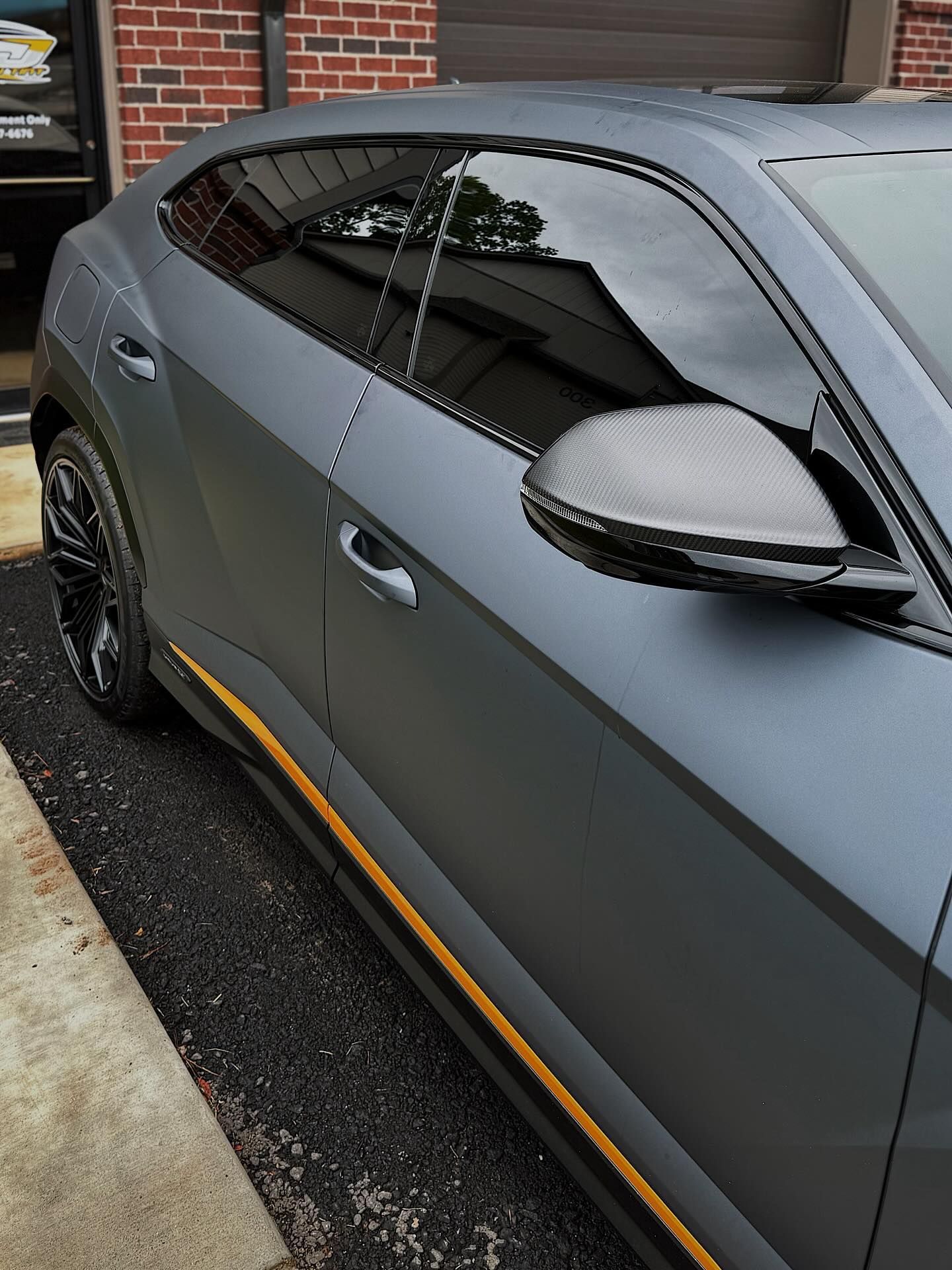 A matte gray Lamborghini Urus parked on a concrete surface, featuring tinted windows and yellow side-skirt accents.