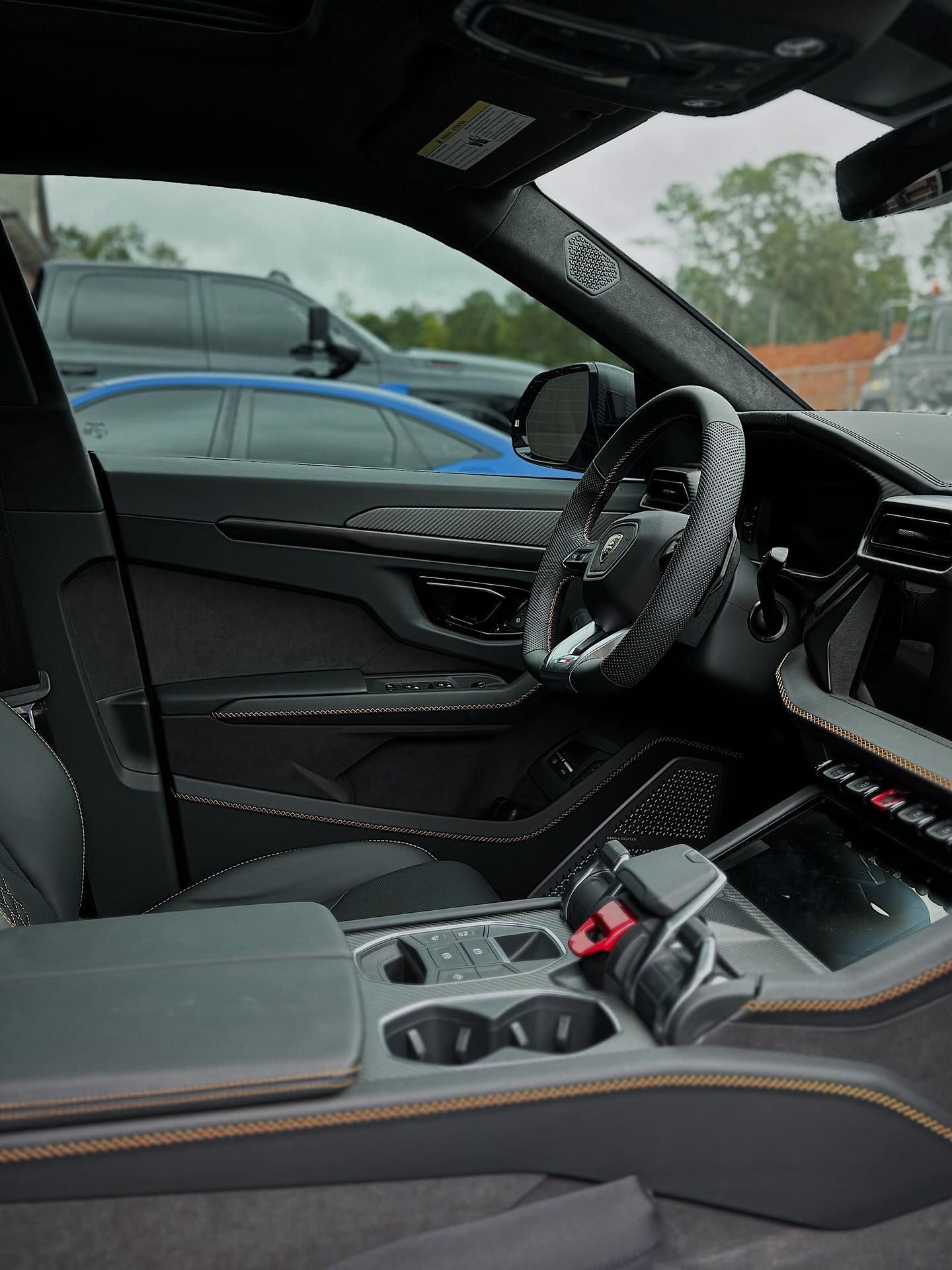 Interior view of a modern luxury car cabin featuring dark upholstery, carbon fiber trim, and a black steering wheel.