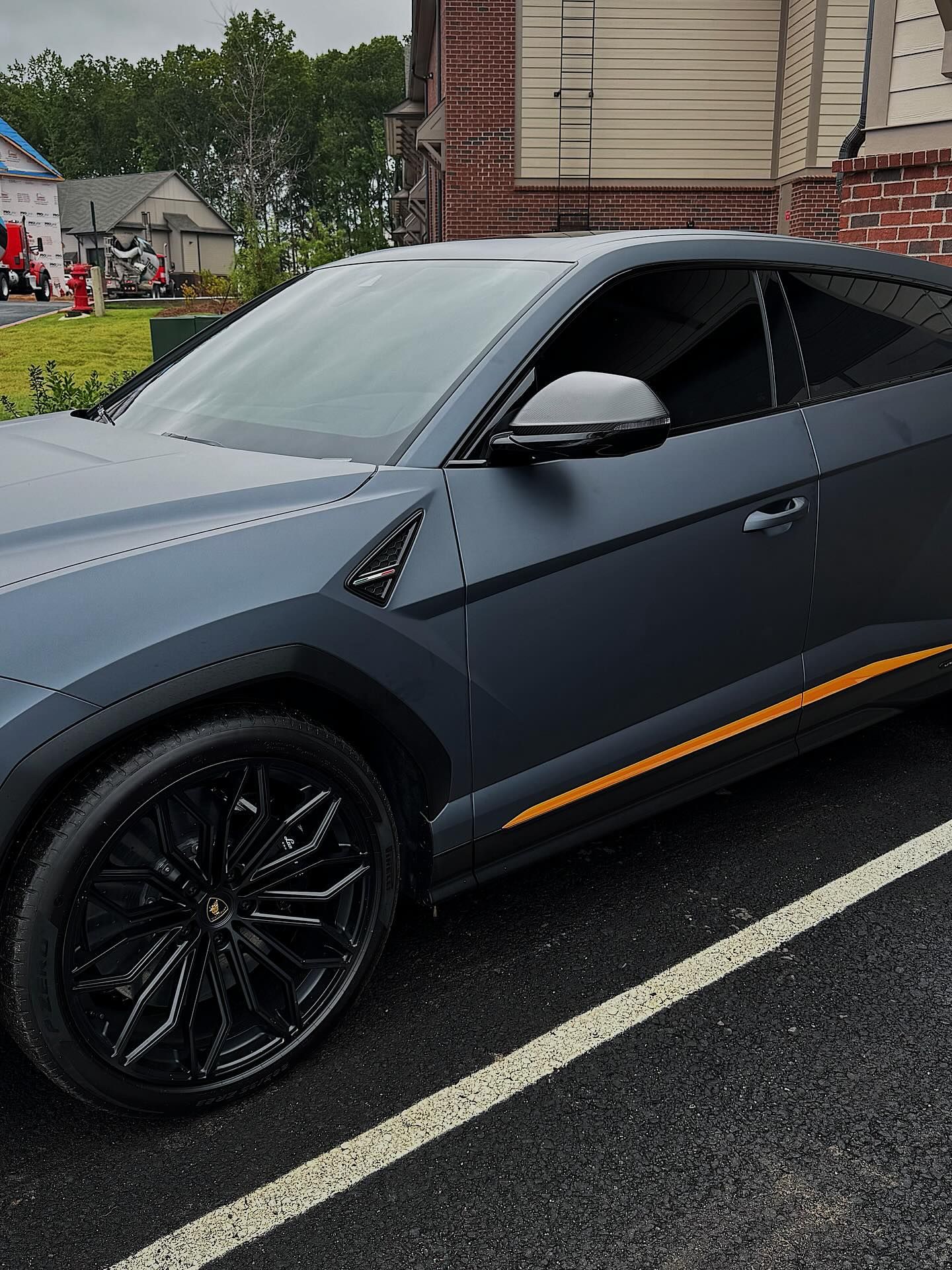 A matte gray Lamborghini Urus with black wheels and a yellow side accent parked on an asphalt lot.