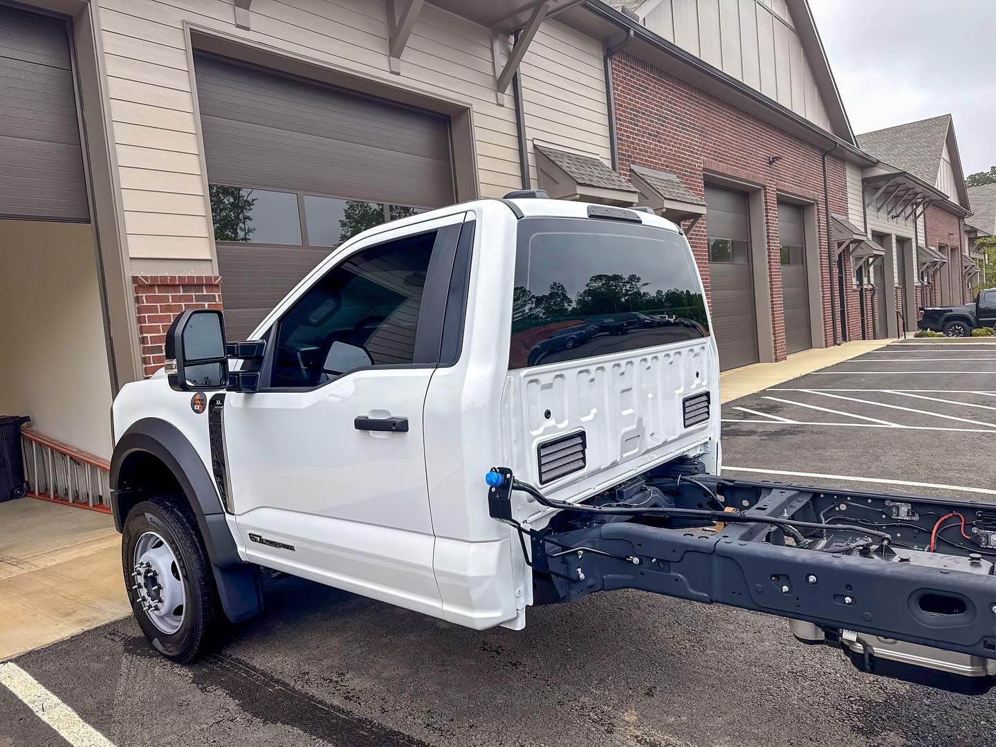 A white Ford Super Duty chassis cab truck parked outside a brick commercial building.