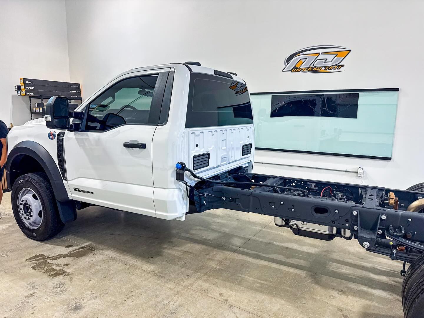 A white Ford F-series cab-chassis truck parked inside a shop with a visible exposed frame.