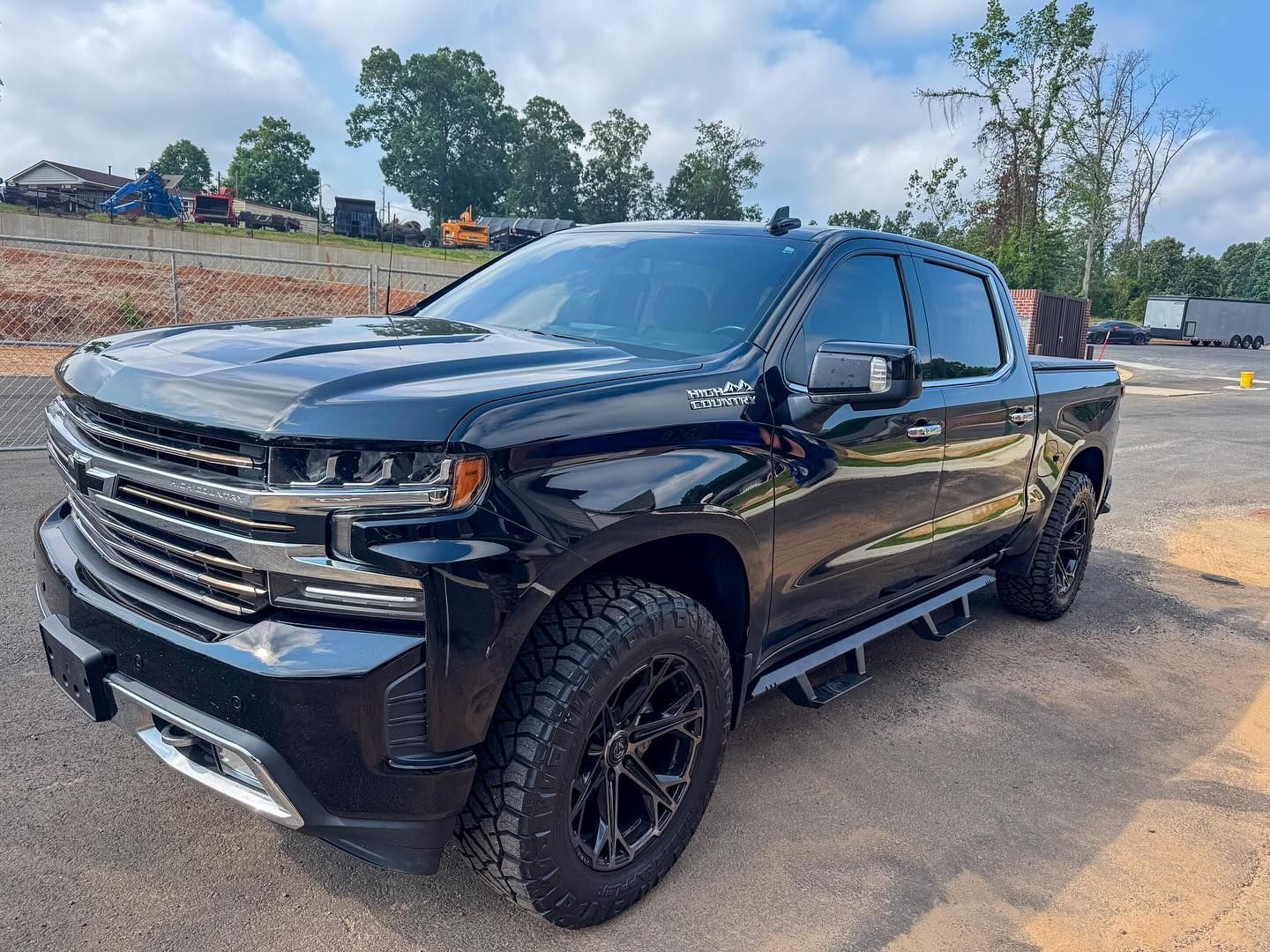 A black Chevrolet Silverado pickup truck parked on a paved lot under a blue sky with light clouds.