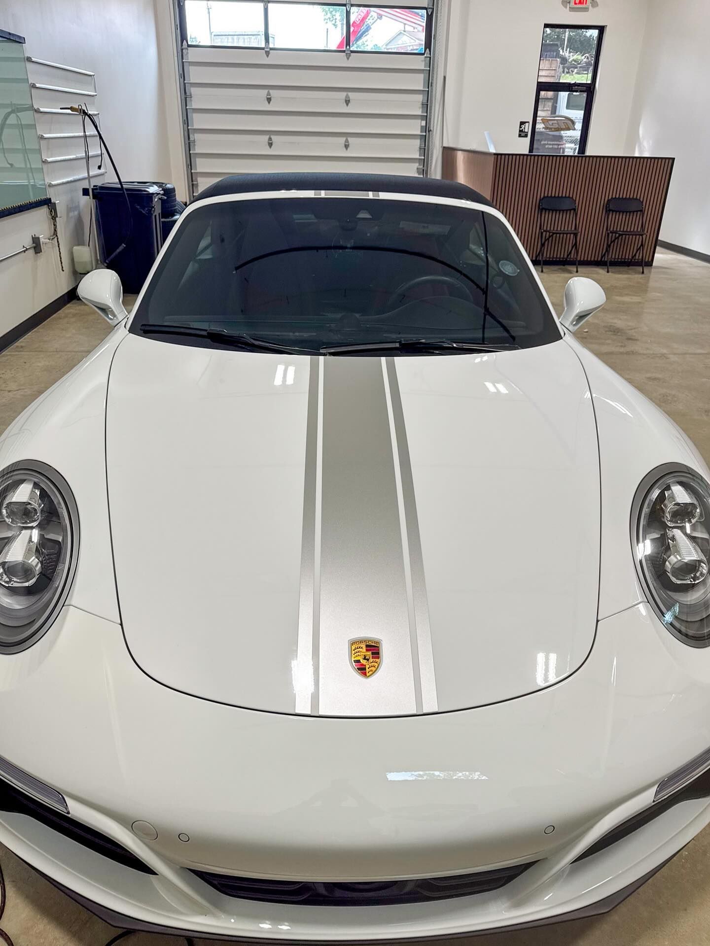 A white Porsche with a silver center racing stripe parked inside a well-lit garage.