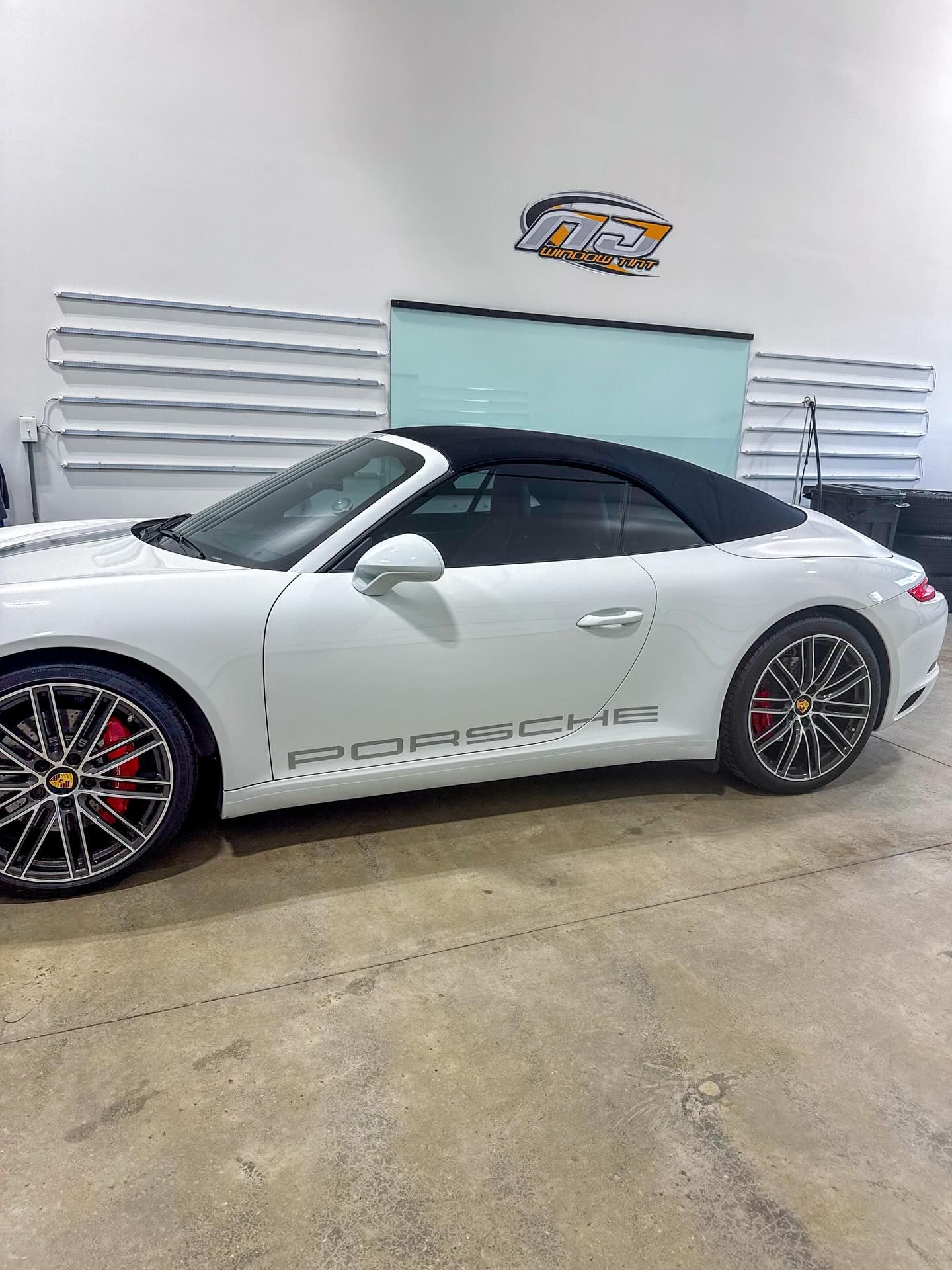 A white Porsche 911 convertible with black soft top and alloy wheels parked inside a garage.