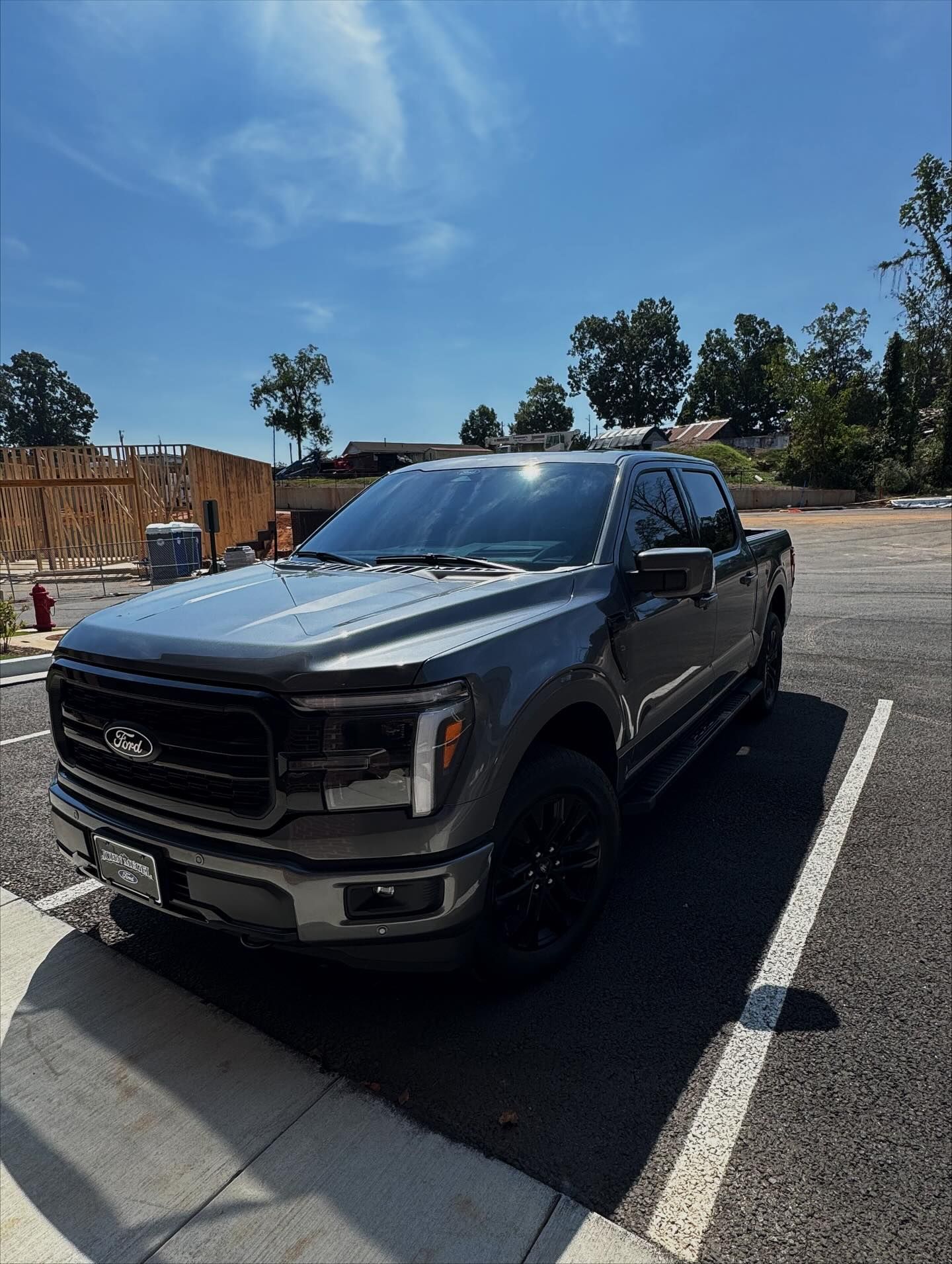 A gray Ford F-150 pickup truck parked in an asphalt parking lot next to a construction site under a clear blue sky.