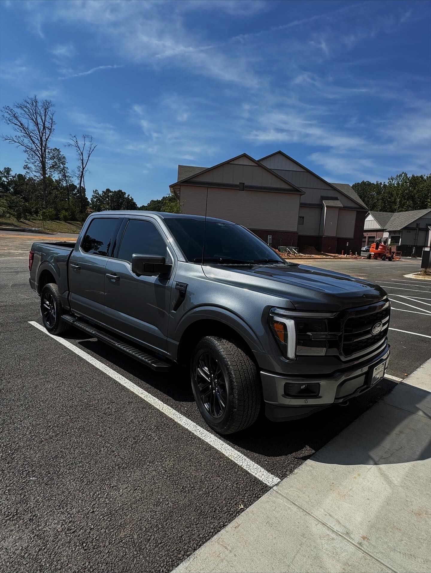 A dark gray Ford F-150 truck parked in an outdoor lot on a sunny day with houses visible in the background.