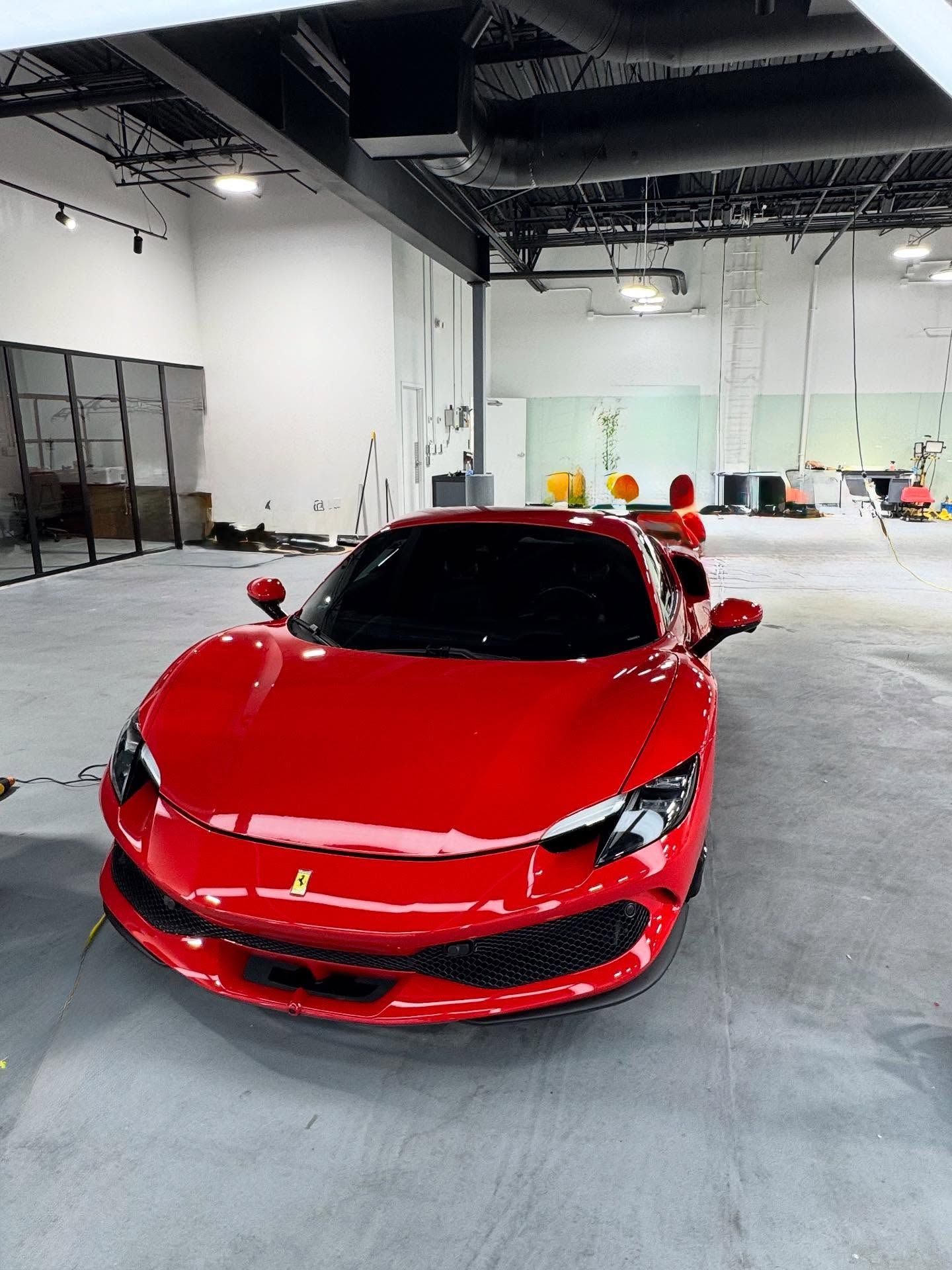 A bright red Ferrari sports car parked in the center of a spacious, modern, industrial-style showroom.
