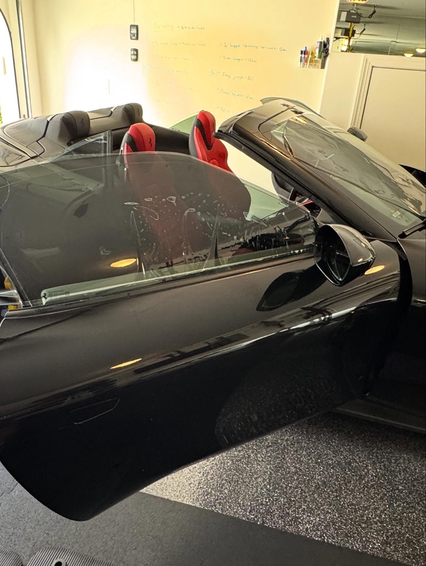 A black convertible car with an open door and bright red interior seats parked in a garage.