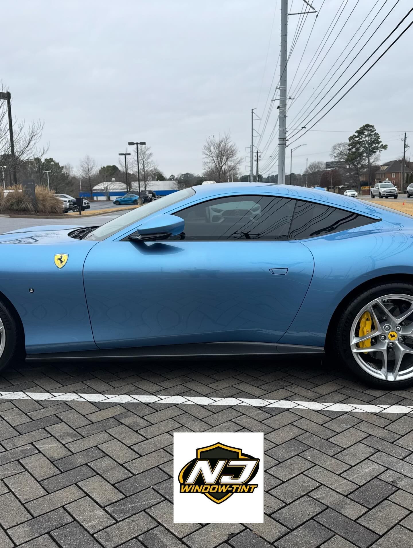 A light blue Ferrari parked on a brick-paved lot with a promotional 