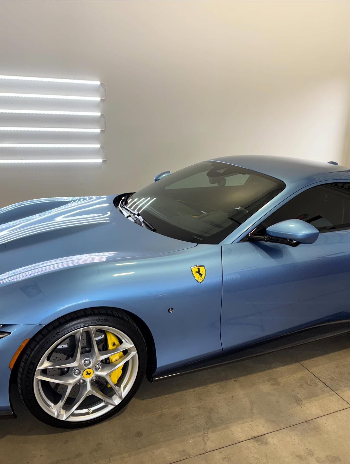 A light blue Ferrari sports car with yellow brake calipers parked in a well-lit indoor garage.