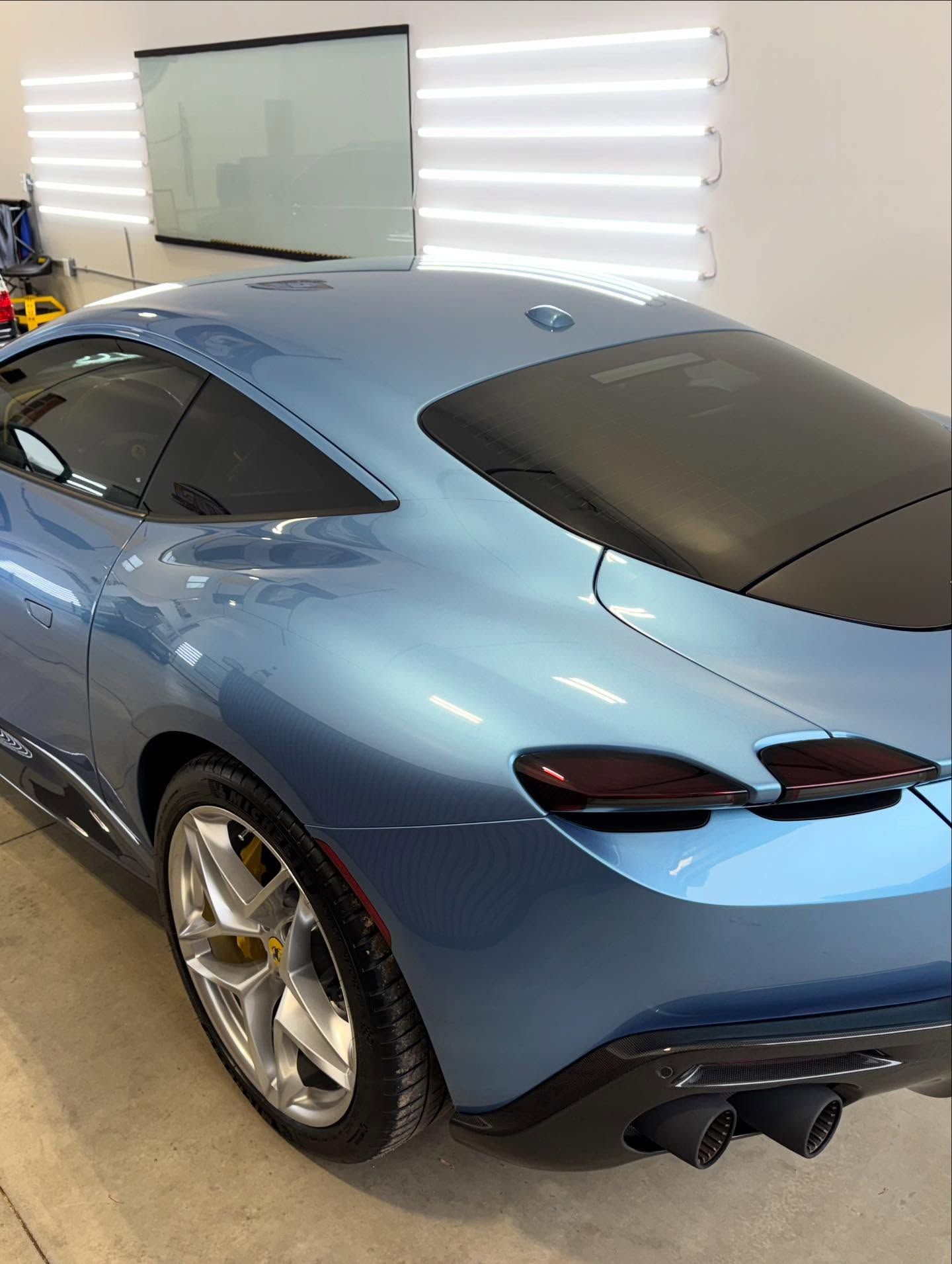 A metallic blue Ferrari Roma sports car parked in a brightly lit professional garage.