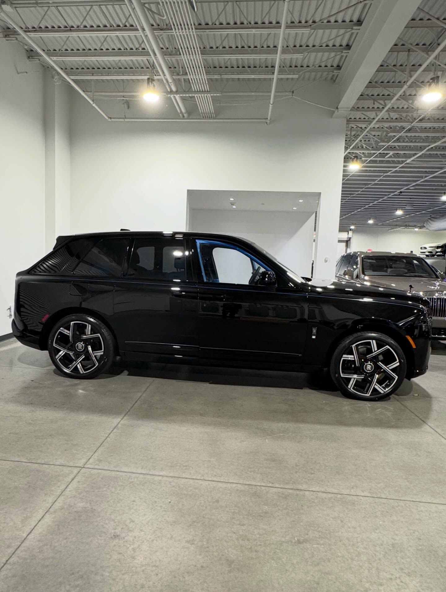 A profile view of a black Rolls-Royce Cullinan SUV parked inside a well-lit showroom with high ceilings.