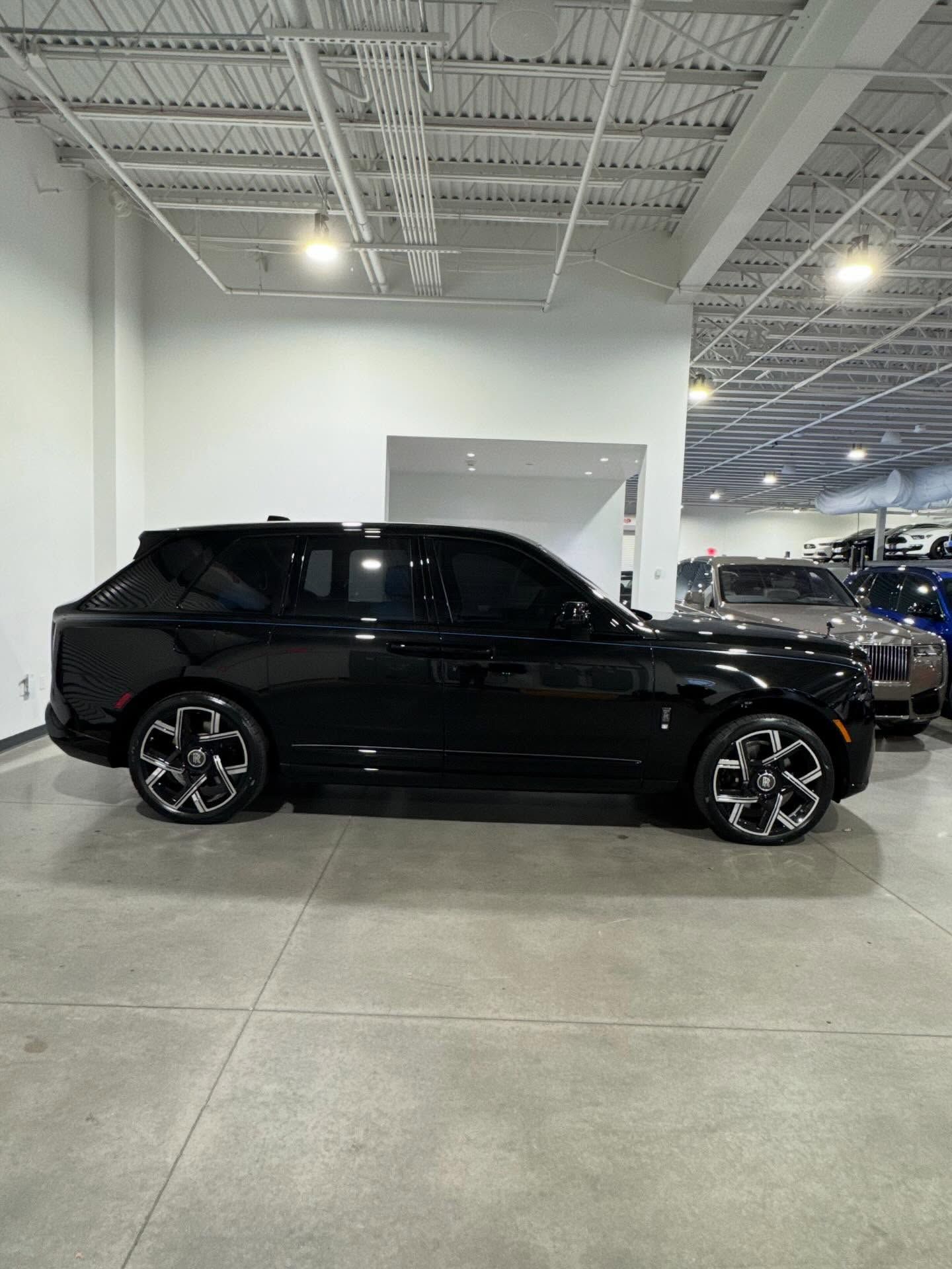 A black Rolls-Royce Cullinan parked inside a brightly lit car dealership showroom.