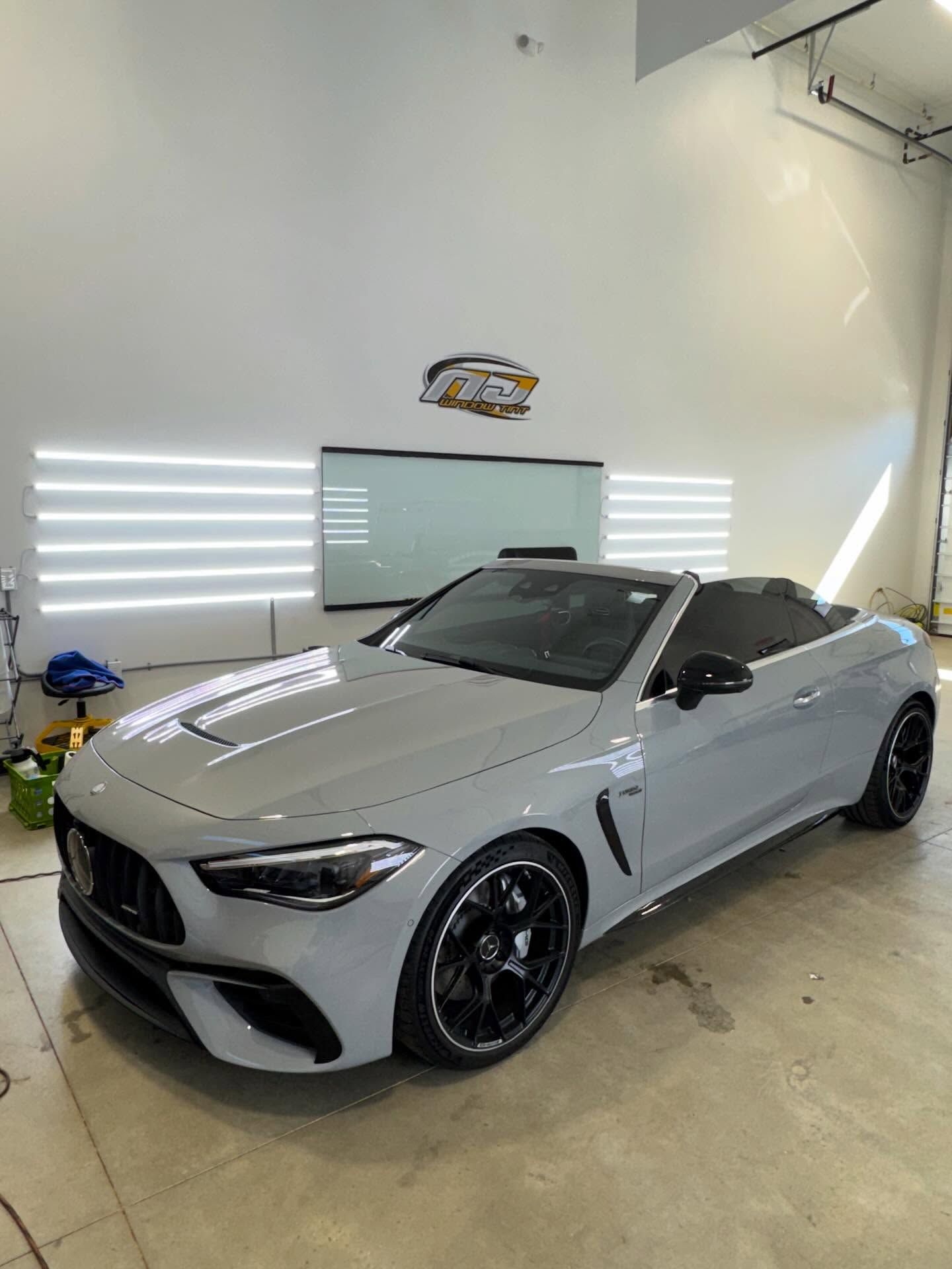 A grey Mercedes-AMG convertible parked in a well-lit, professional garage with linear wall lighting.