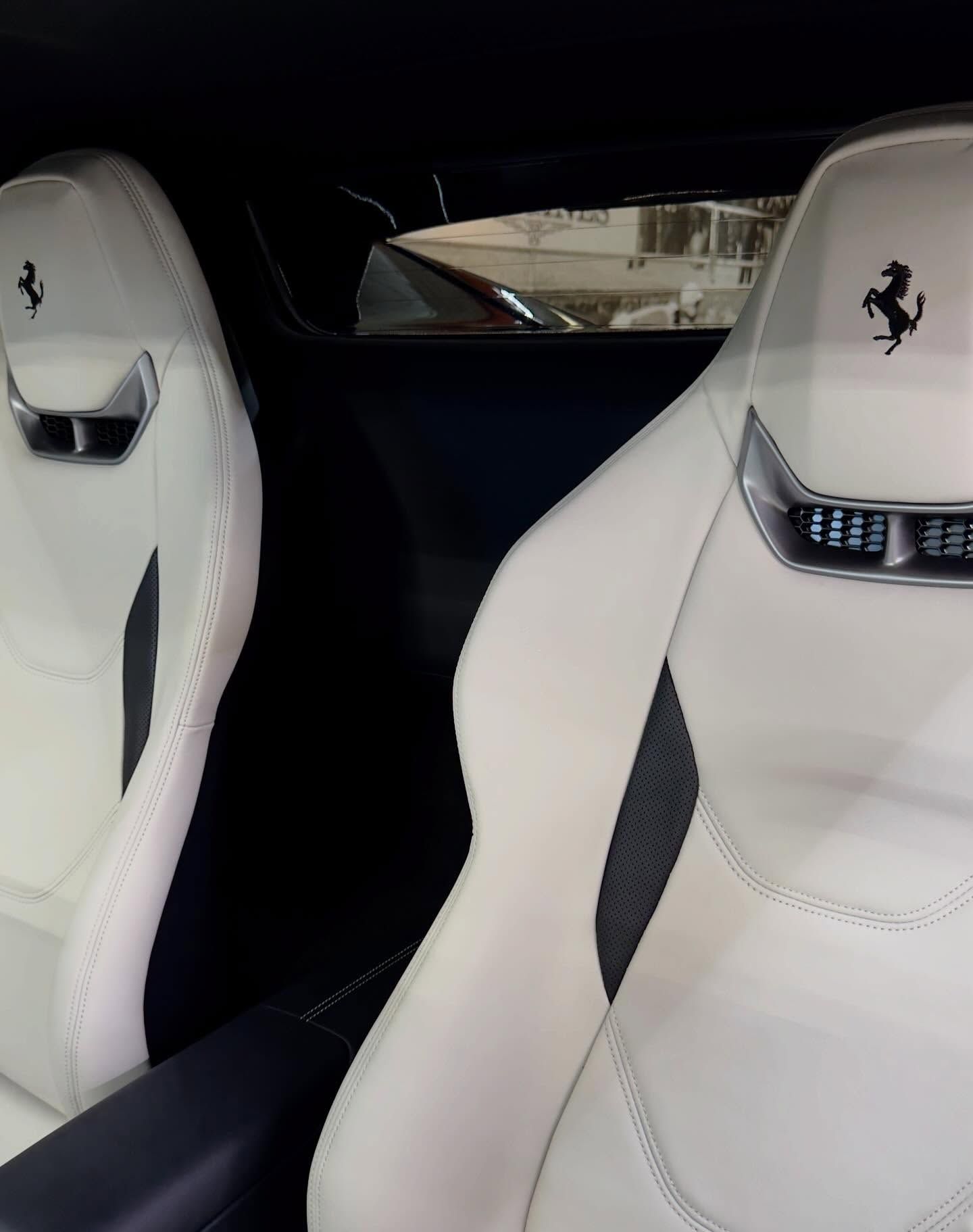 Interior of a car featuring two white leather bucket seats with black accents and Ferrari emblems on the headrests.