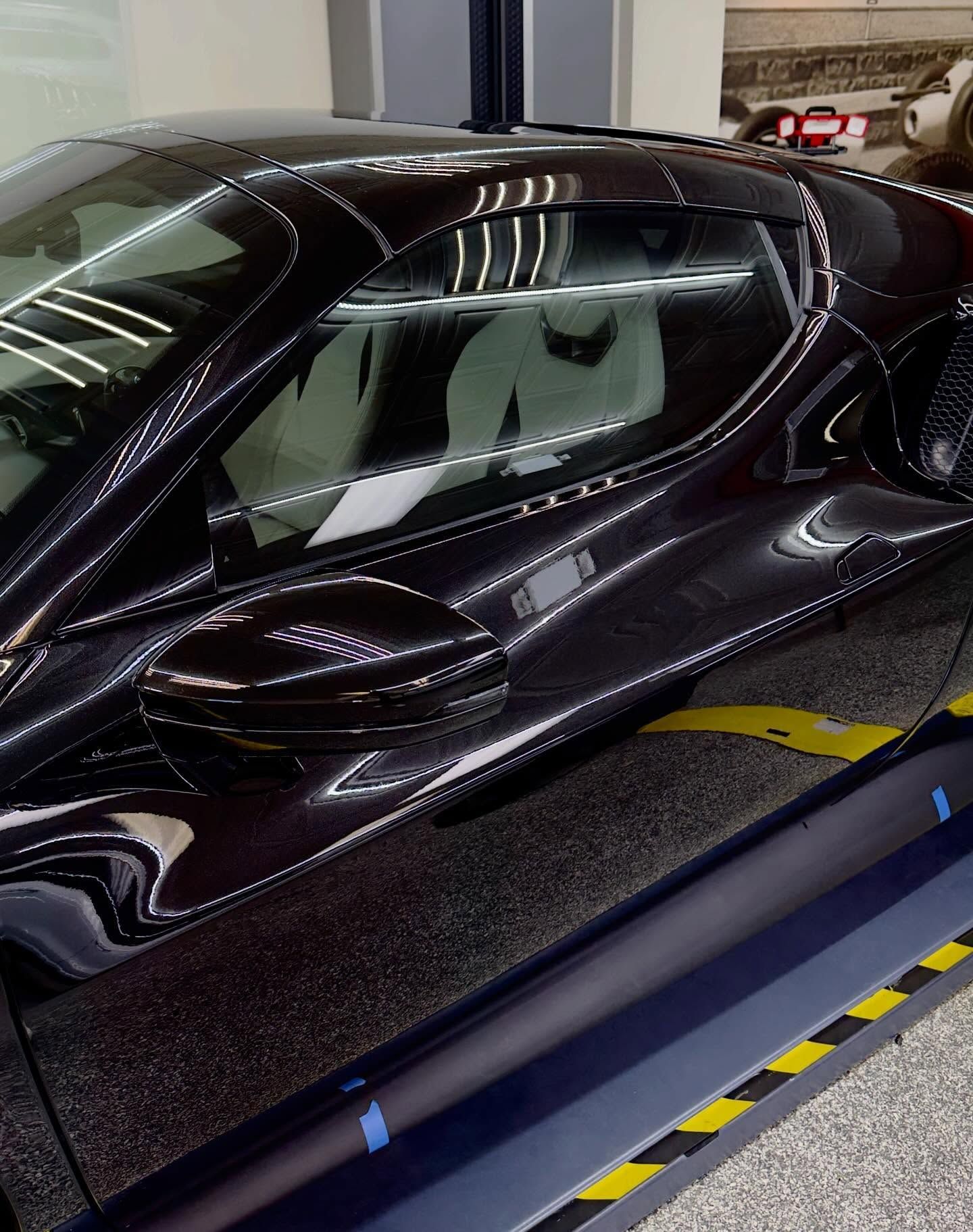 A sleek, dark-colored sports car parked indoors on a surface with yellow safety striping.