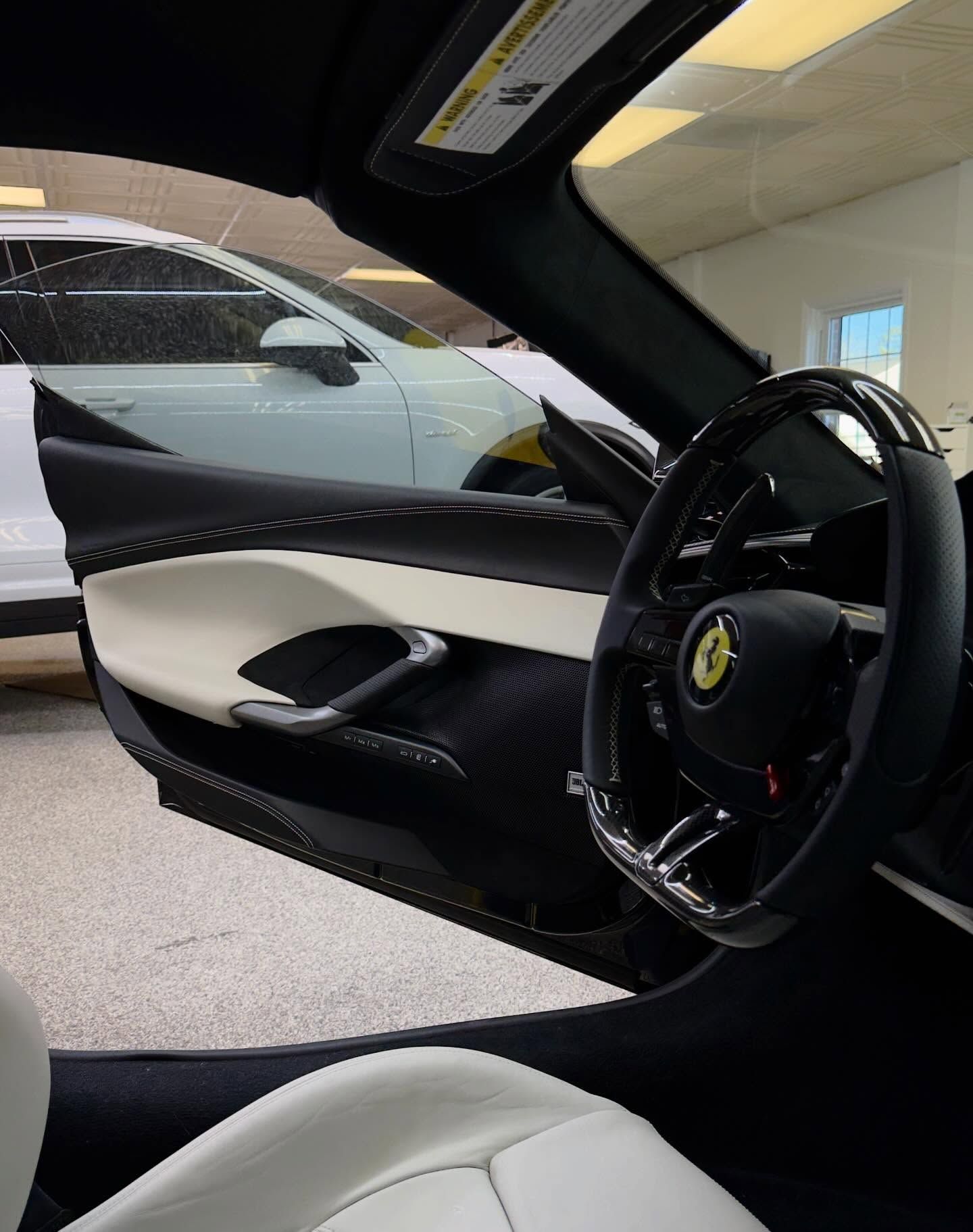 Interior view of a black and white Ferrari cockpit showing the steering wheel, dashboard, and open door.