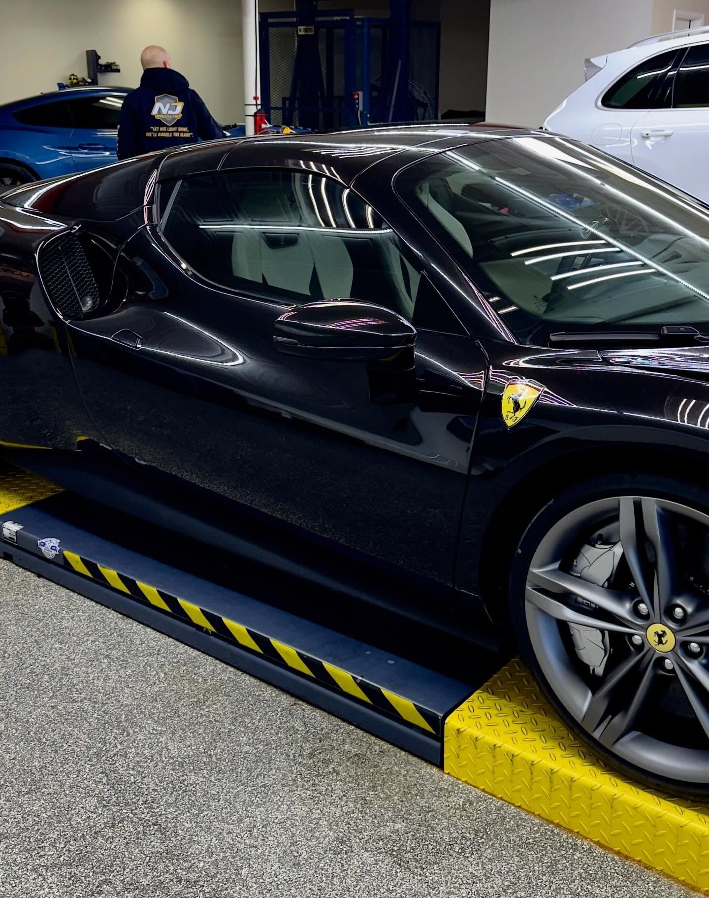 A black Ferrari sports car parked on a service lift inside an automotive shop.