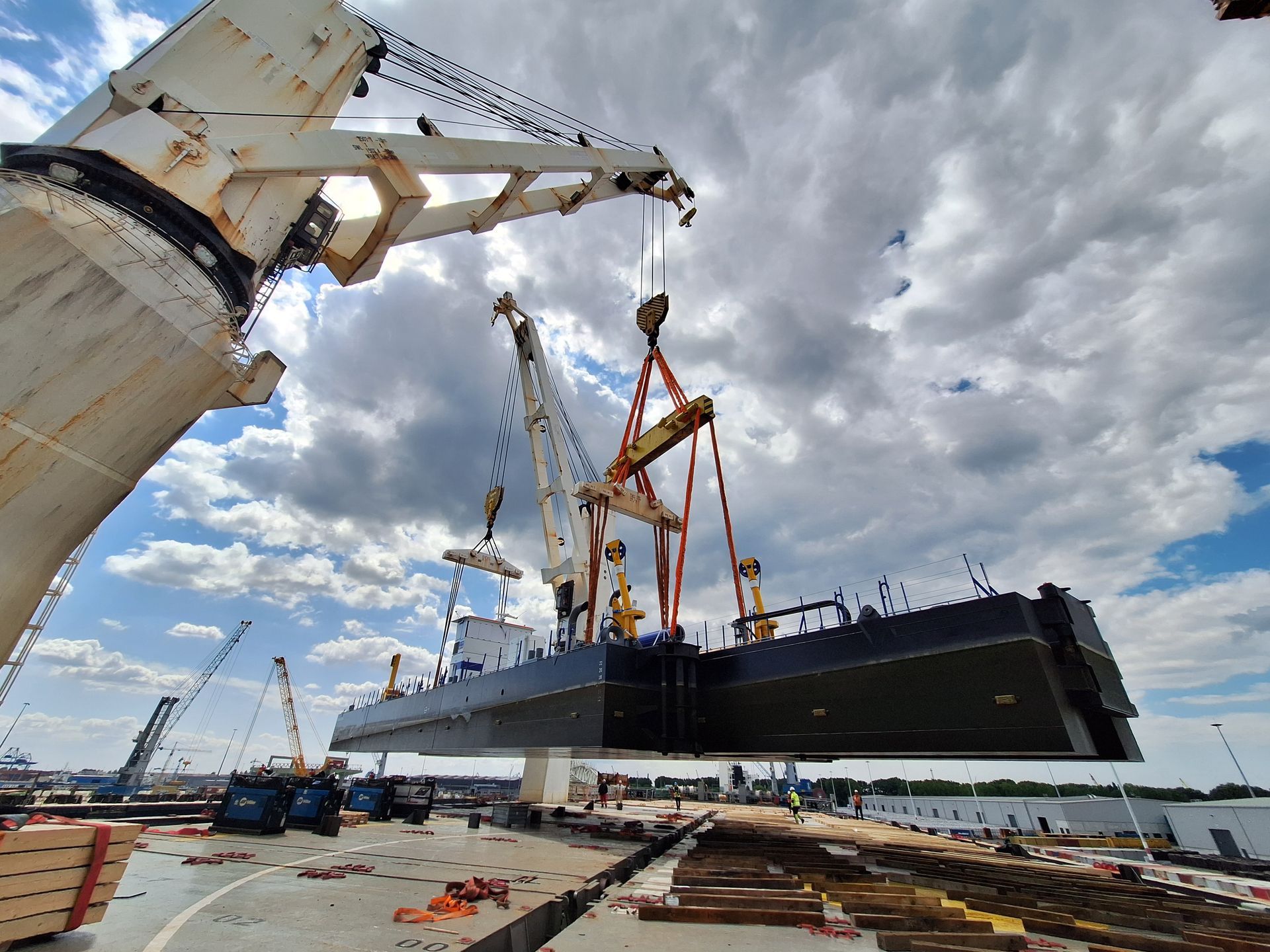 Large ship segment being lifted by cranes at a dock. Sky is cloudy. Van Karsen Heavy Lift marine surveys and P&I support