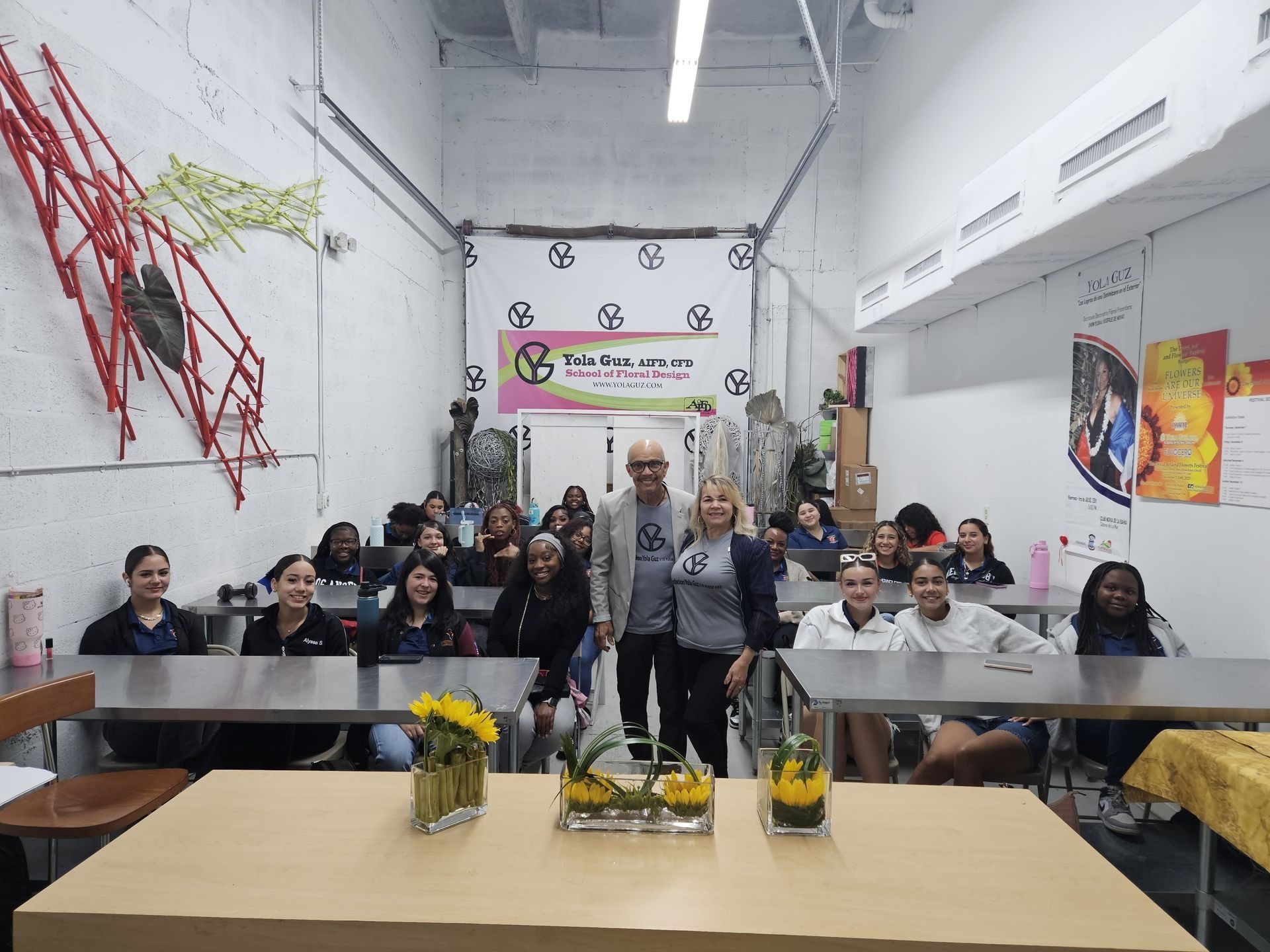 People seated at tables in a bright classroom, facing the camera with a banner at the front.