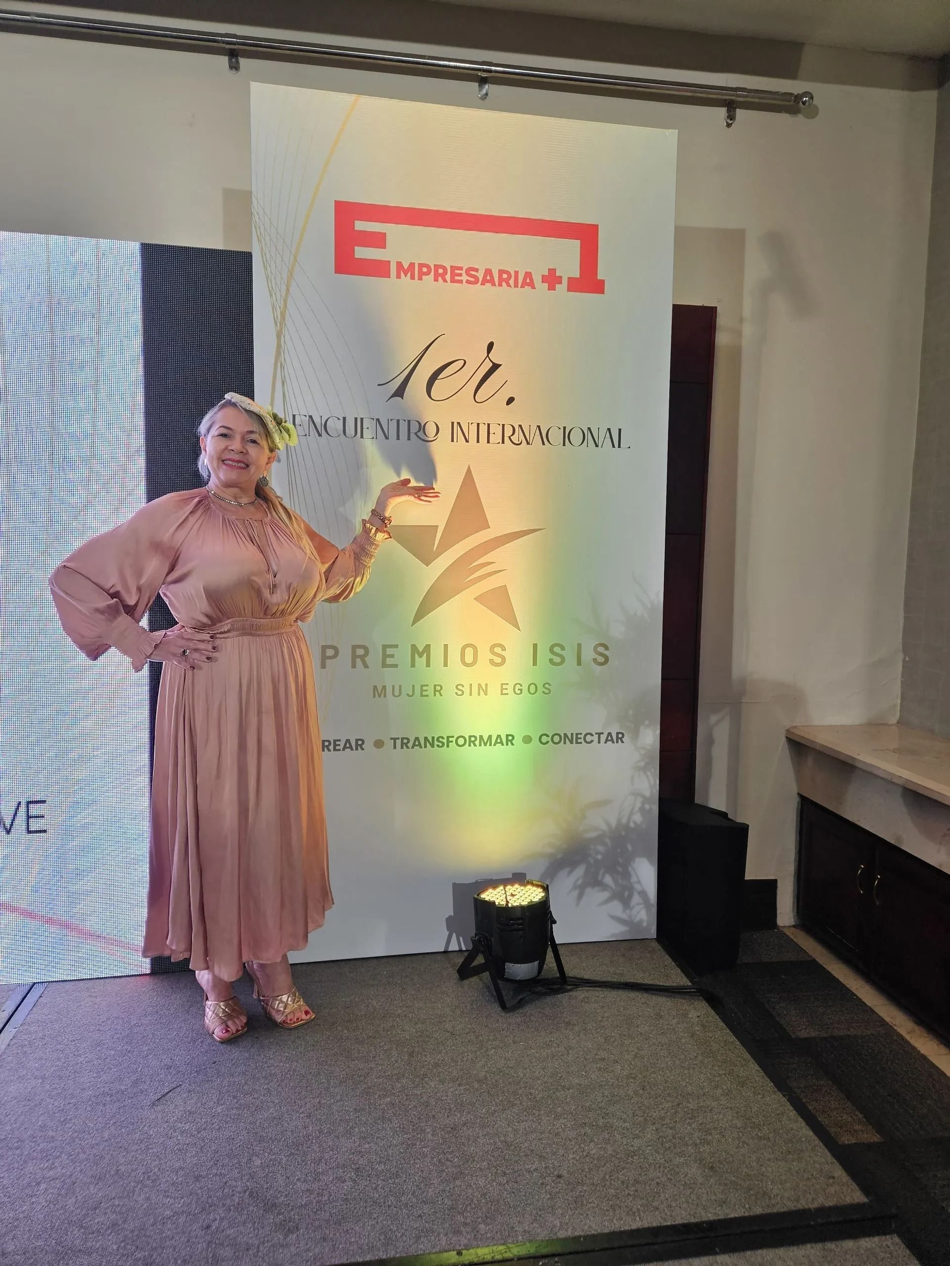 Woman in a pink dress standing beside a branded event banner in an indoor venue