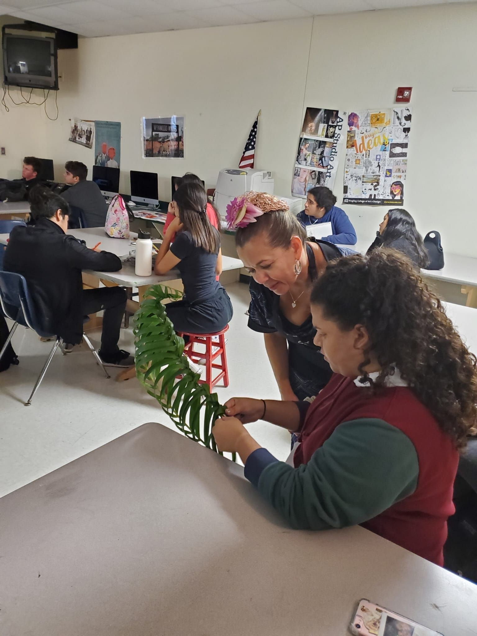People seated at tables in a classroom, chatting and working on crafts and papers.