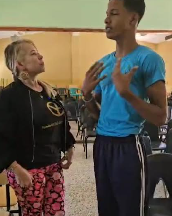 Two people standing indoors, talking; one gestures with hands while the other listens.